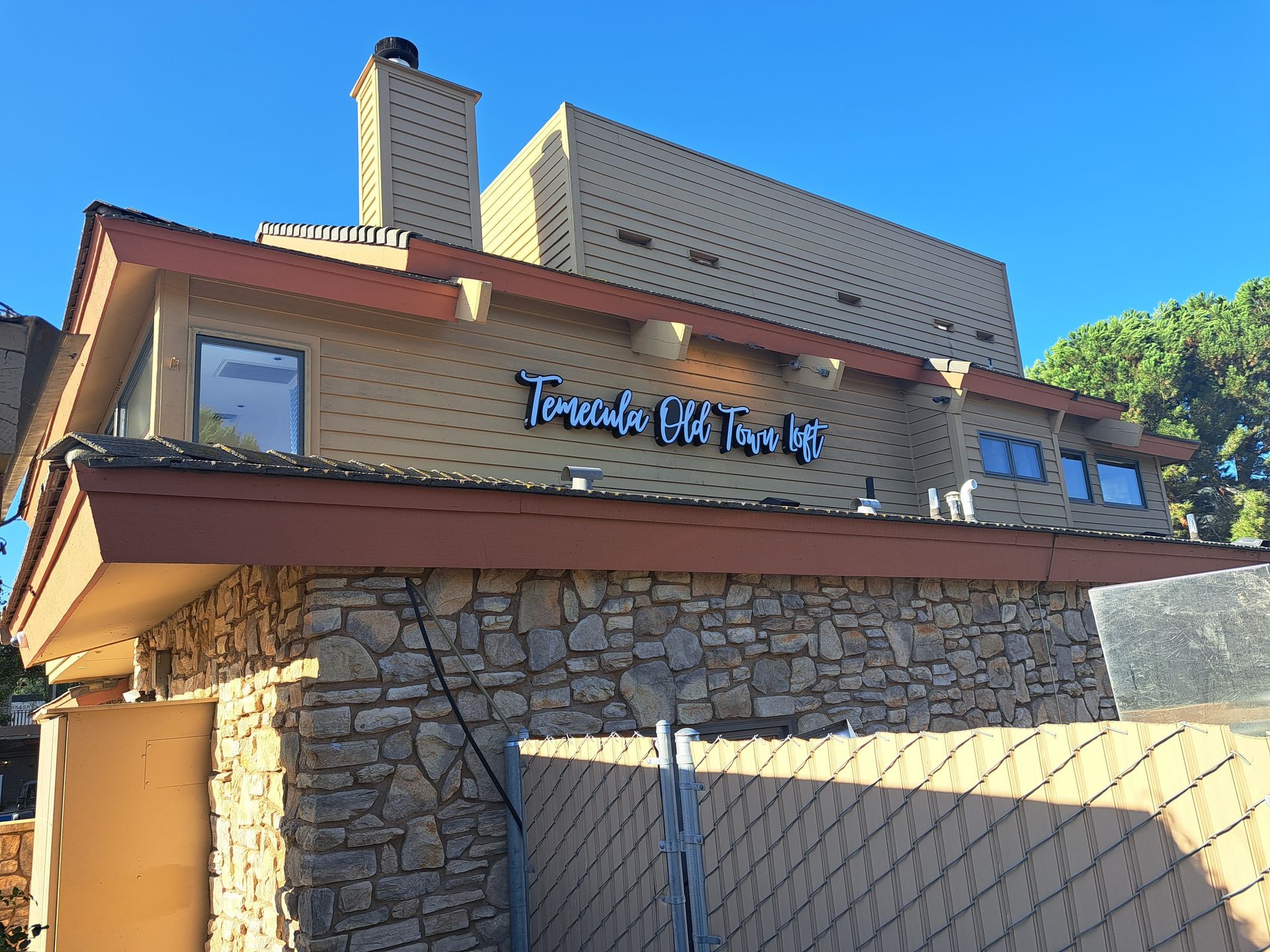 Stone-and-wood building with a metal sign on the front, viewed from below in bright sunlight.