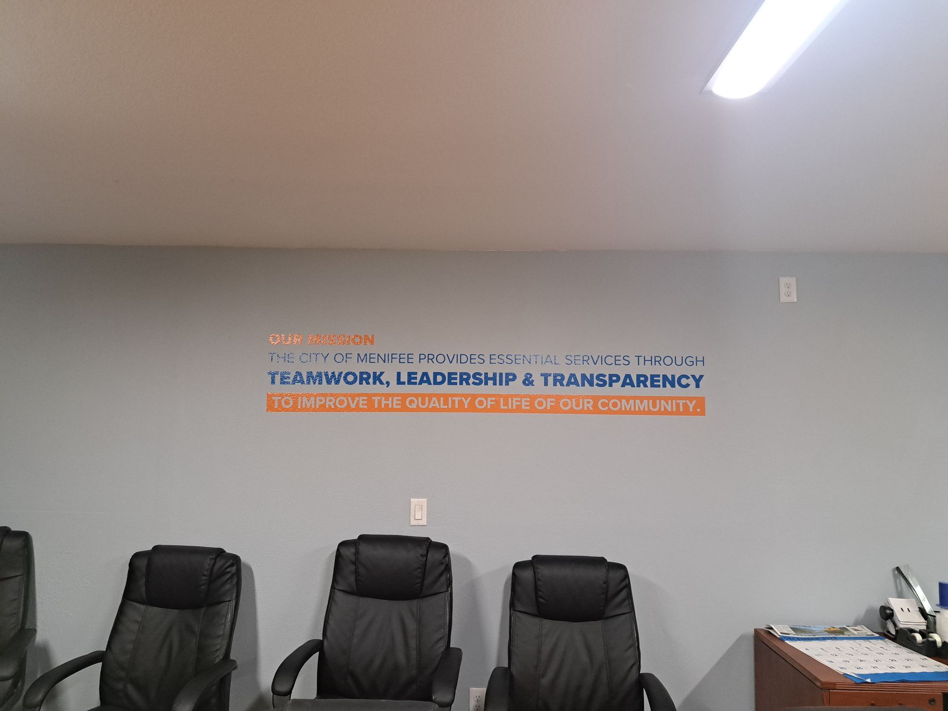 Office wall with motivational text above three black chairs and a desk in the corner