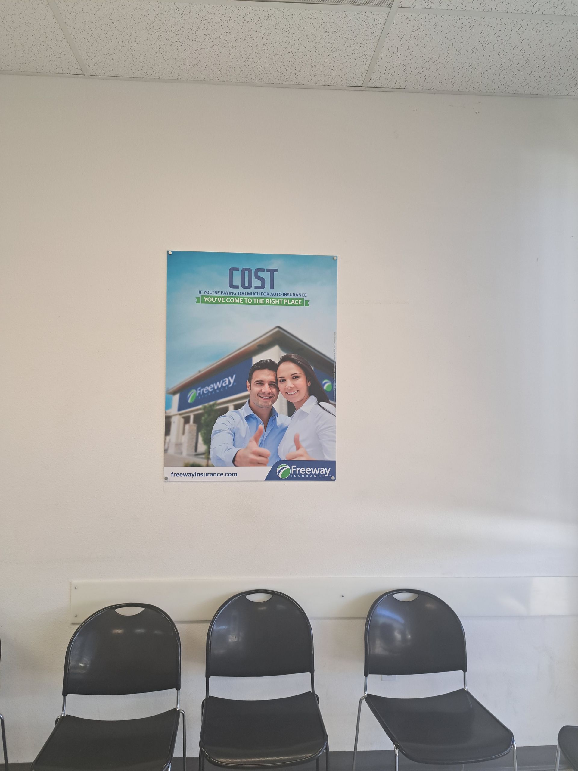 Waiting area with three black chairs beneath a wall poster above a white ledge.