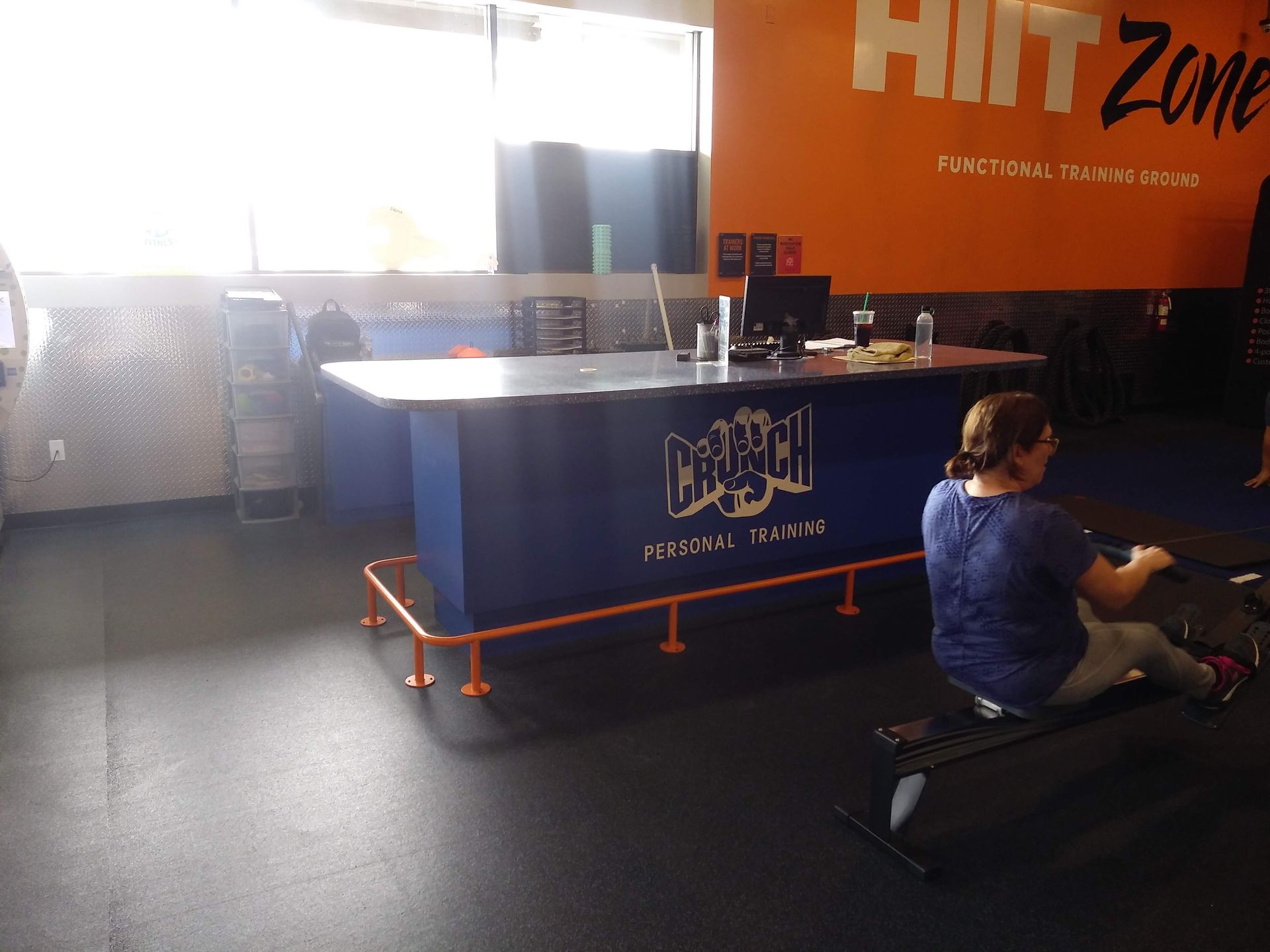 Person stretching on a bench in a gym with a ping-pong table and orange wall in the background