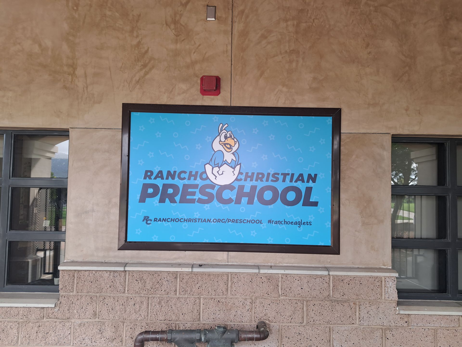 Baptist Christian Preschool sign on a blue screen mounted on a beige building wall.