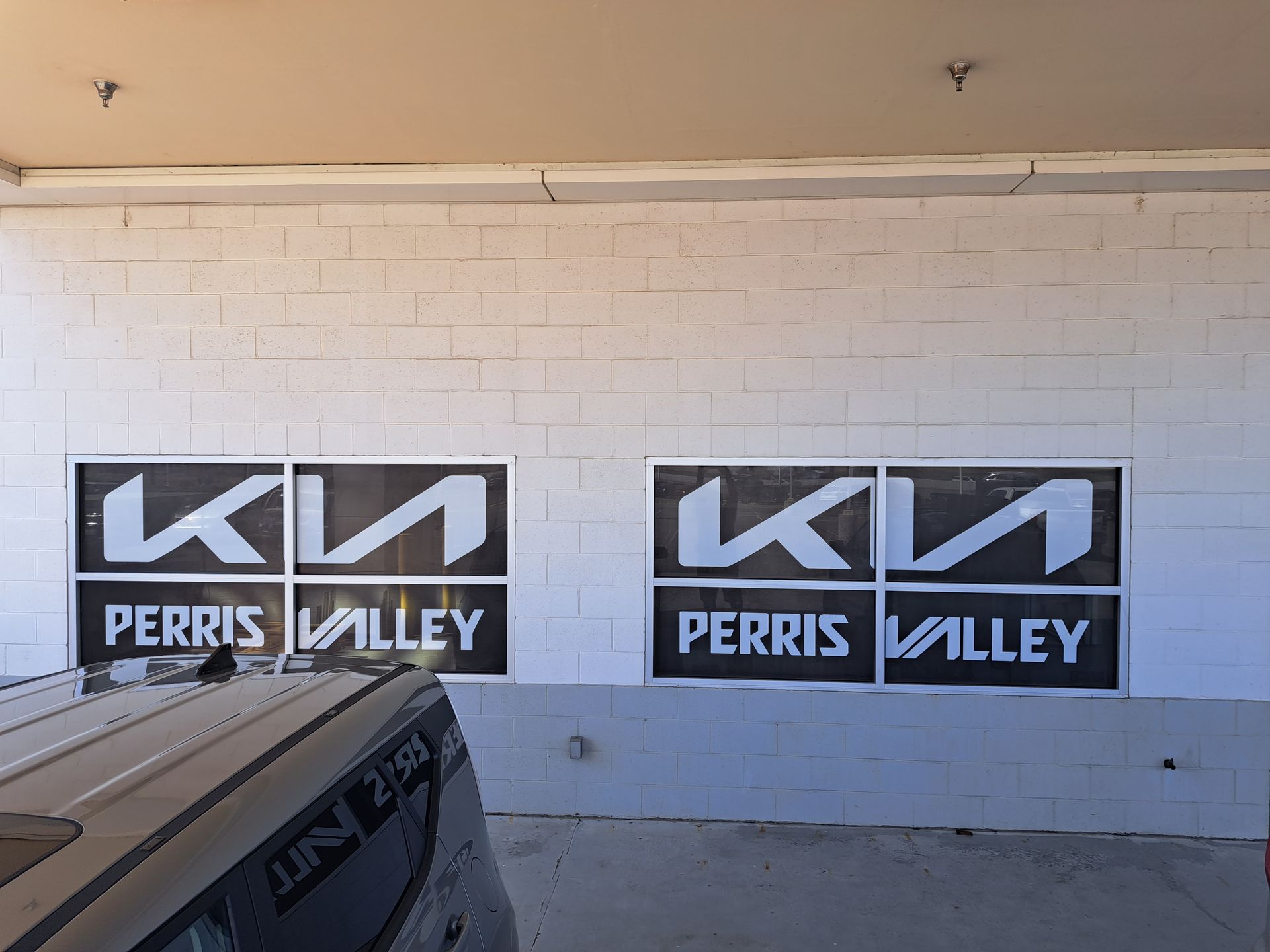 Two black and white Kia Perris Valley signs on a white brick wall under an overhang.