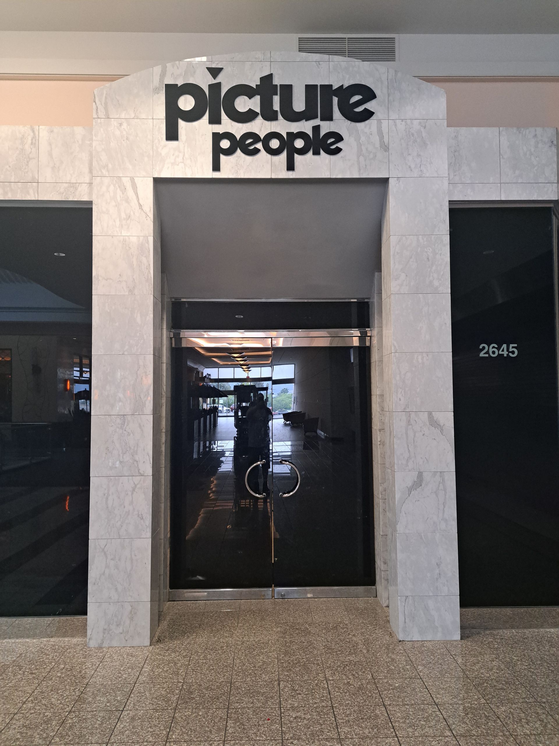 Storefront with “picture people” sign above a glass entrance at a shopping center.