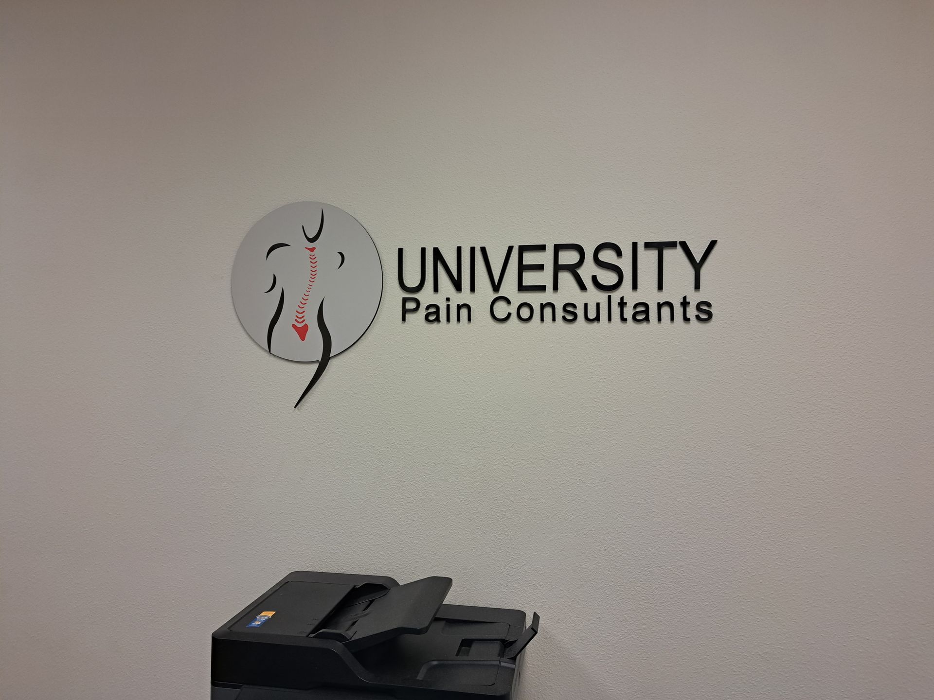 University Pain Consultants logo on a wall above a printer