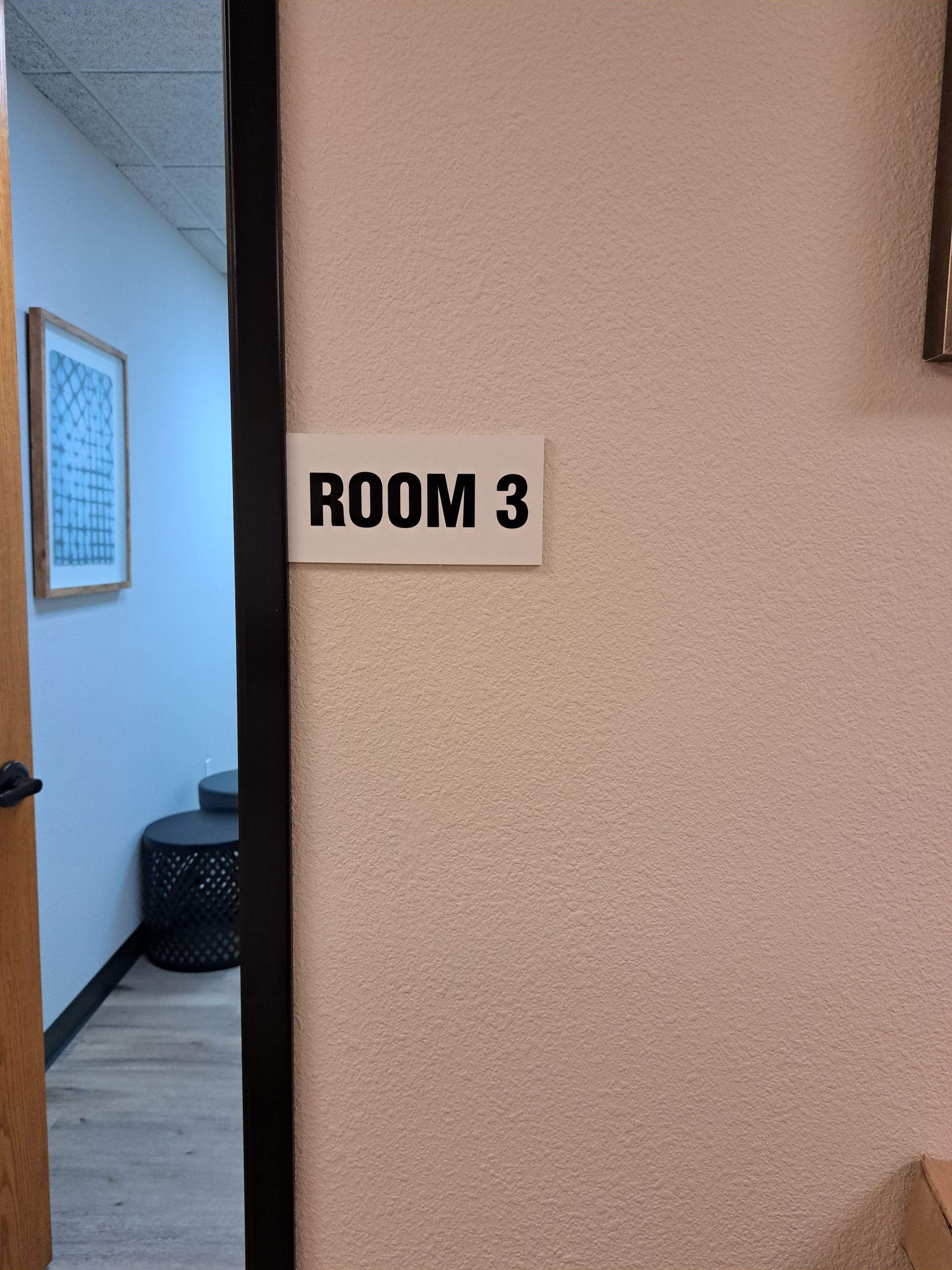 White wall sign reading “ROOM 3” beside a doorway into a blue room