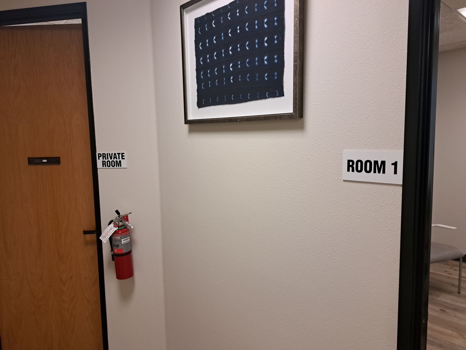 Hallway wall with door, fire extinguisher, and “ROOM 1” sign outside a room.