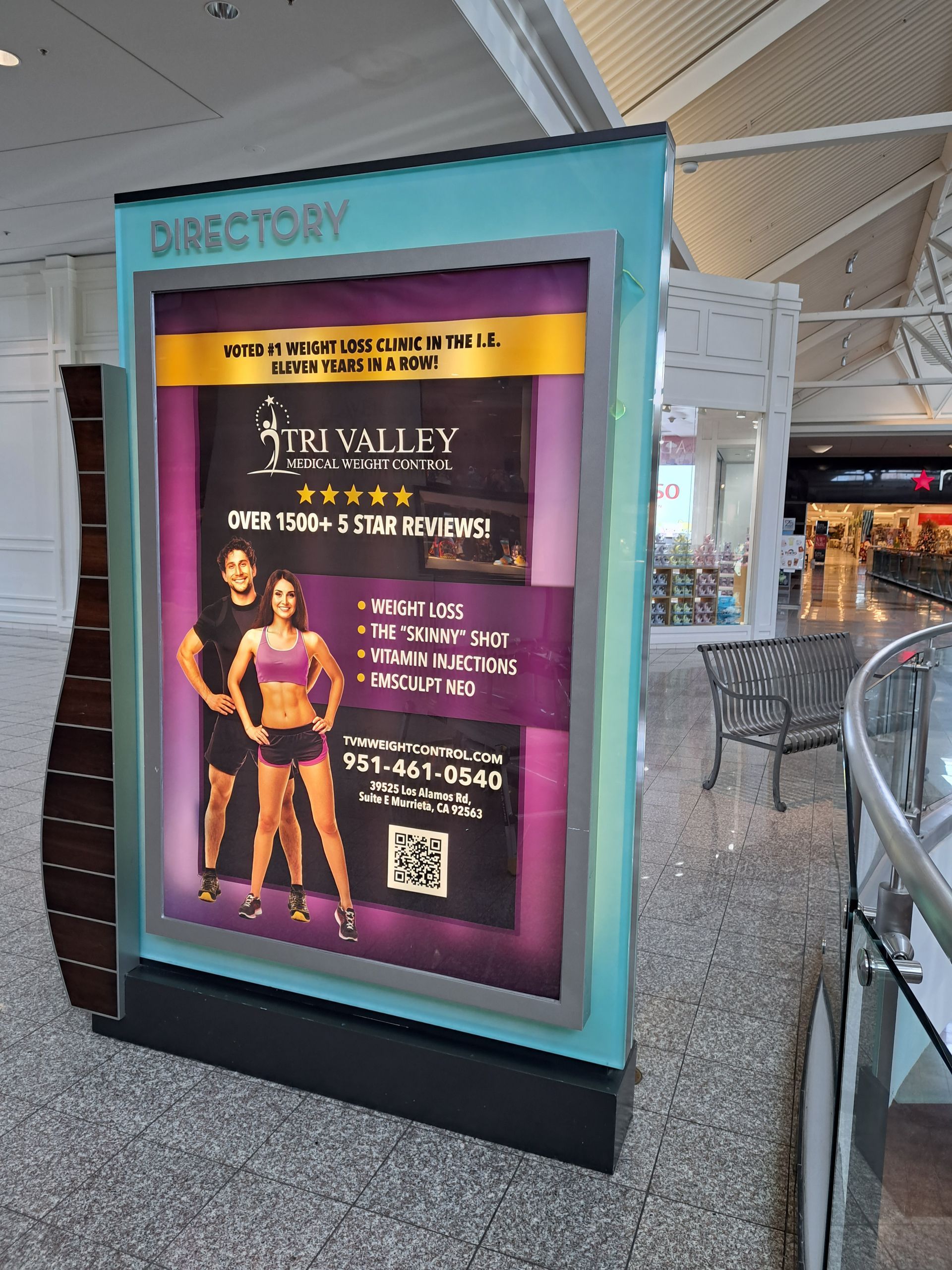 Mall directory kiosk with purple event poster and QR code in a mall corridor