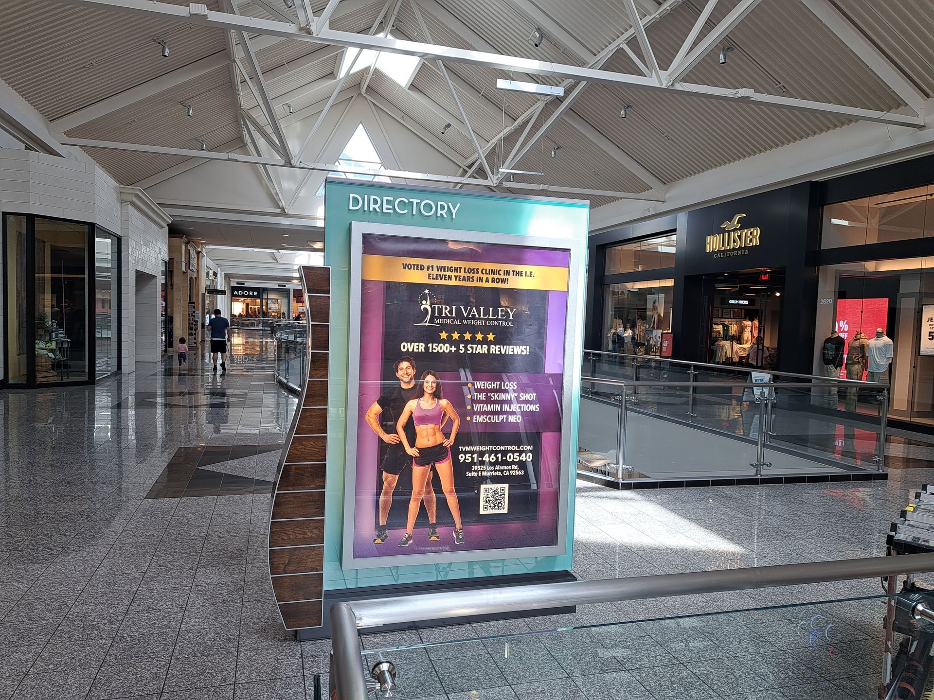 Mall directory sign in a shopping mall corridor with a colorful event poster.