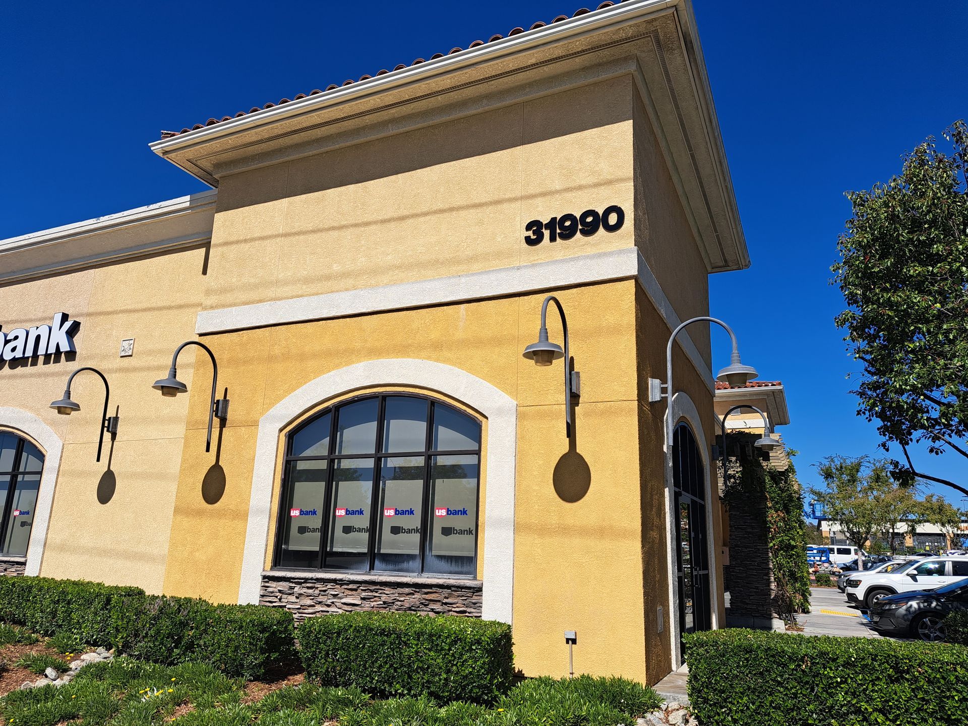 Yellow stucco bank building with arched window and address 31900 under a blue sky