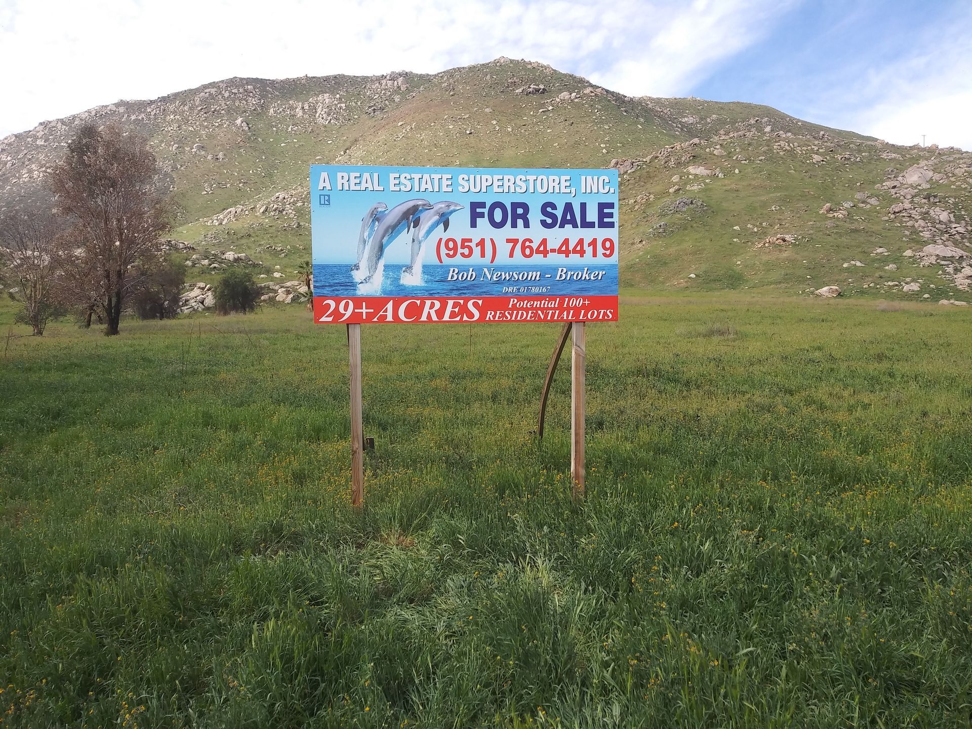 For sale sign in a grassy field with hills in the background and a phone number.