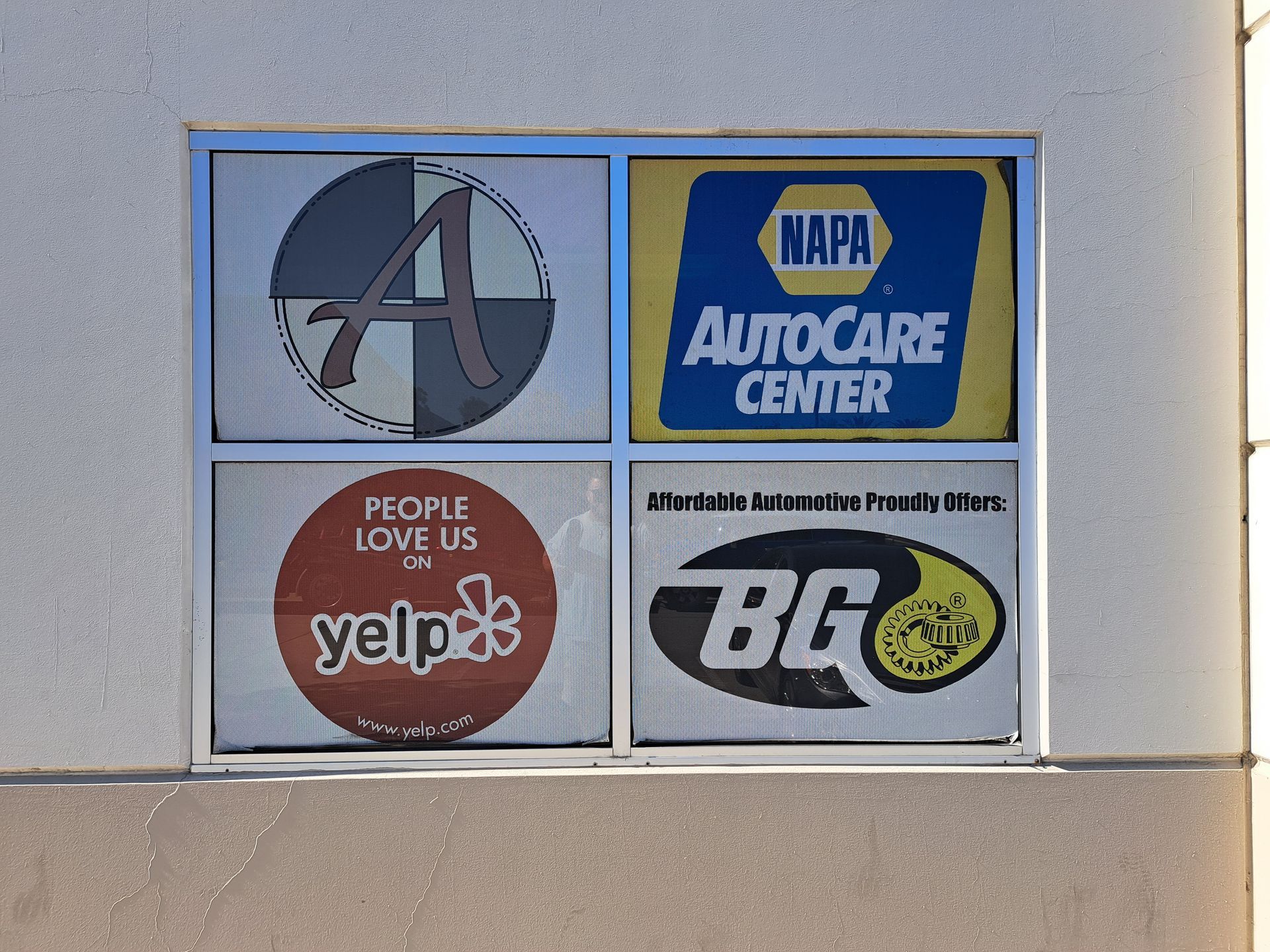 Four business logos on a building wall: 4, NAPA AutoCare Center, Yelp, and BG Products.