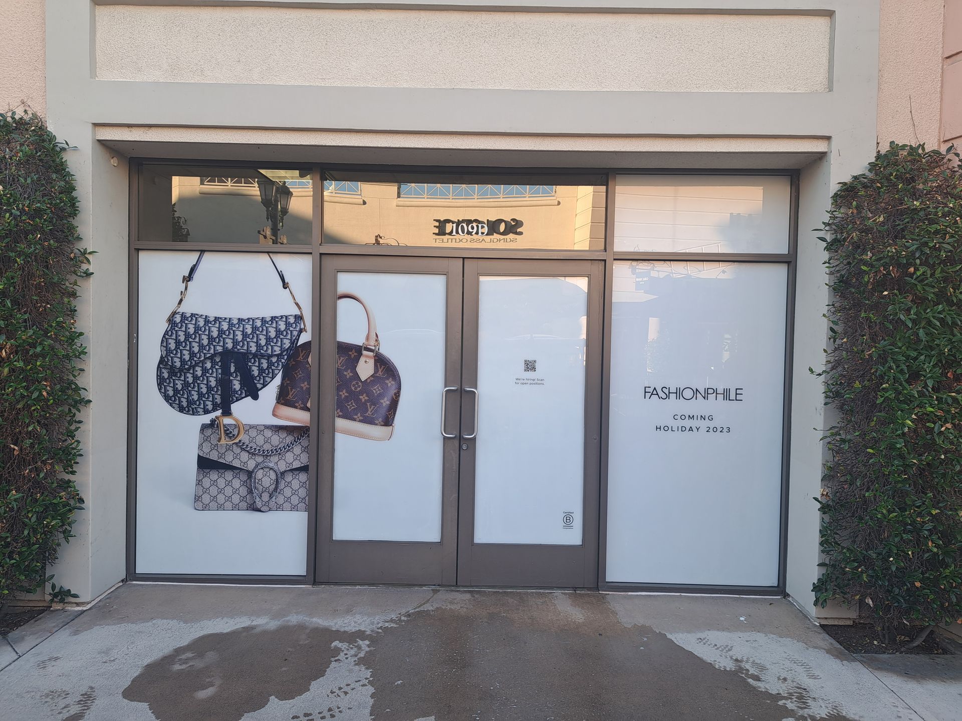 Storefront with frosted glass doors and fashion imagery, framed by ivy on both sides.