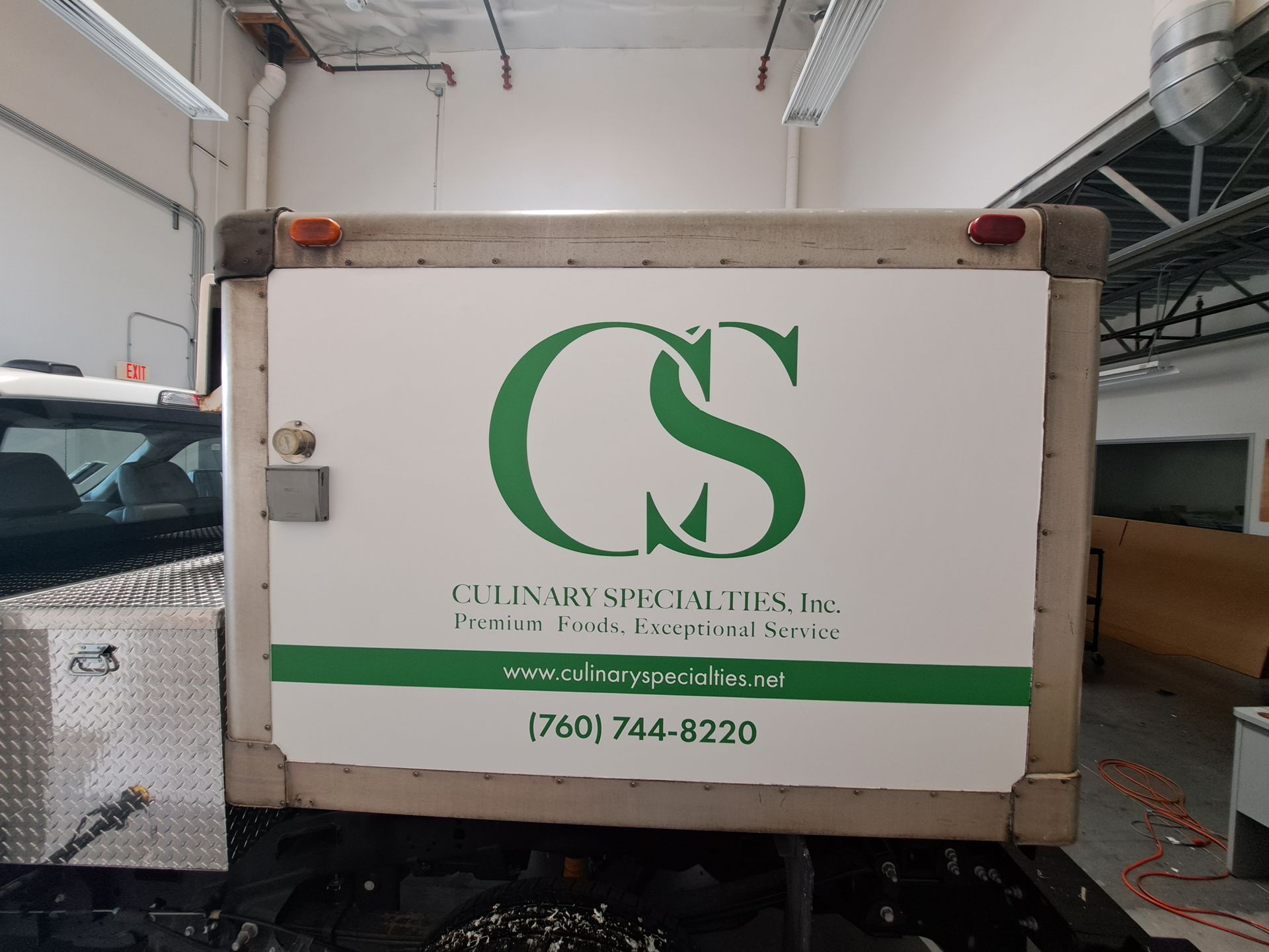 White CS delivery truck with green logo and phone number inside a warehouse.