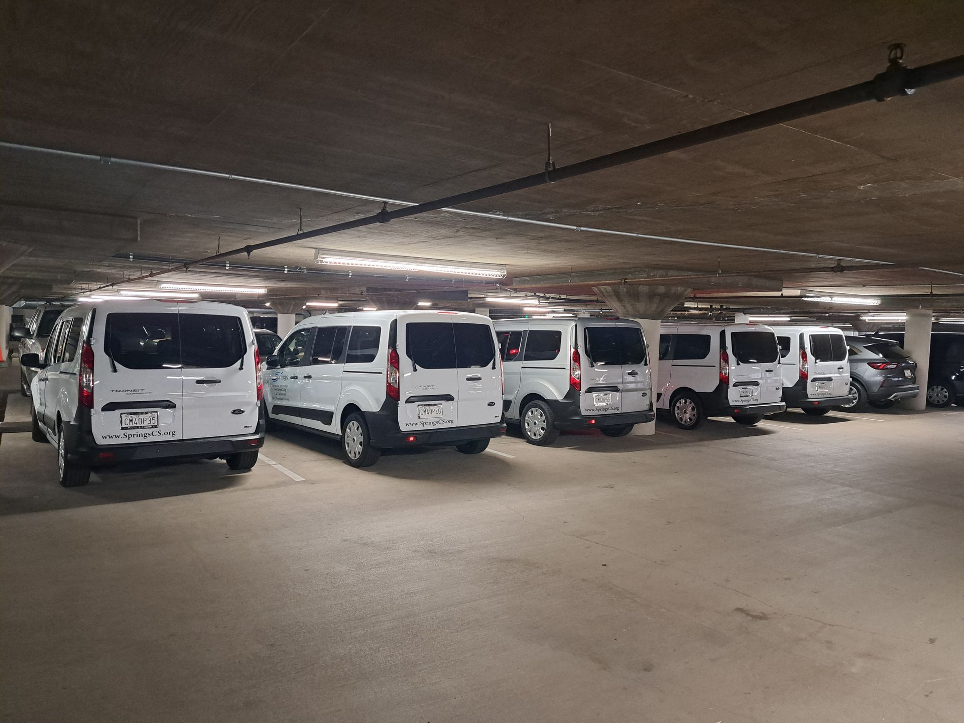 Parking garage with several white vans parked in rows under fluorescent lighting