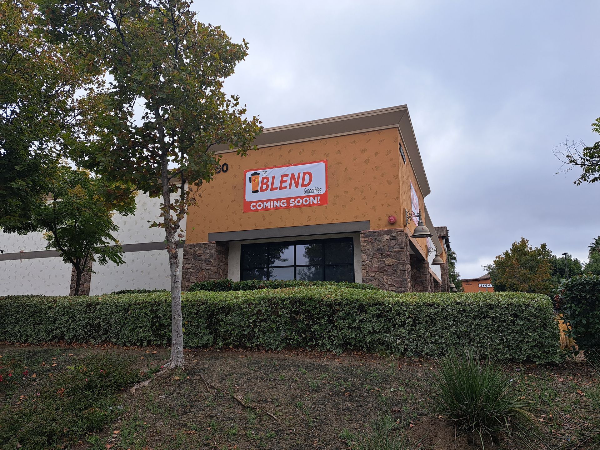 ILBEI sign on a tan corner building behind hedges and a tree under a cloudy sky