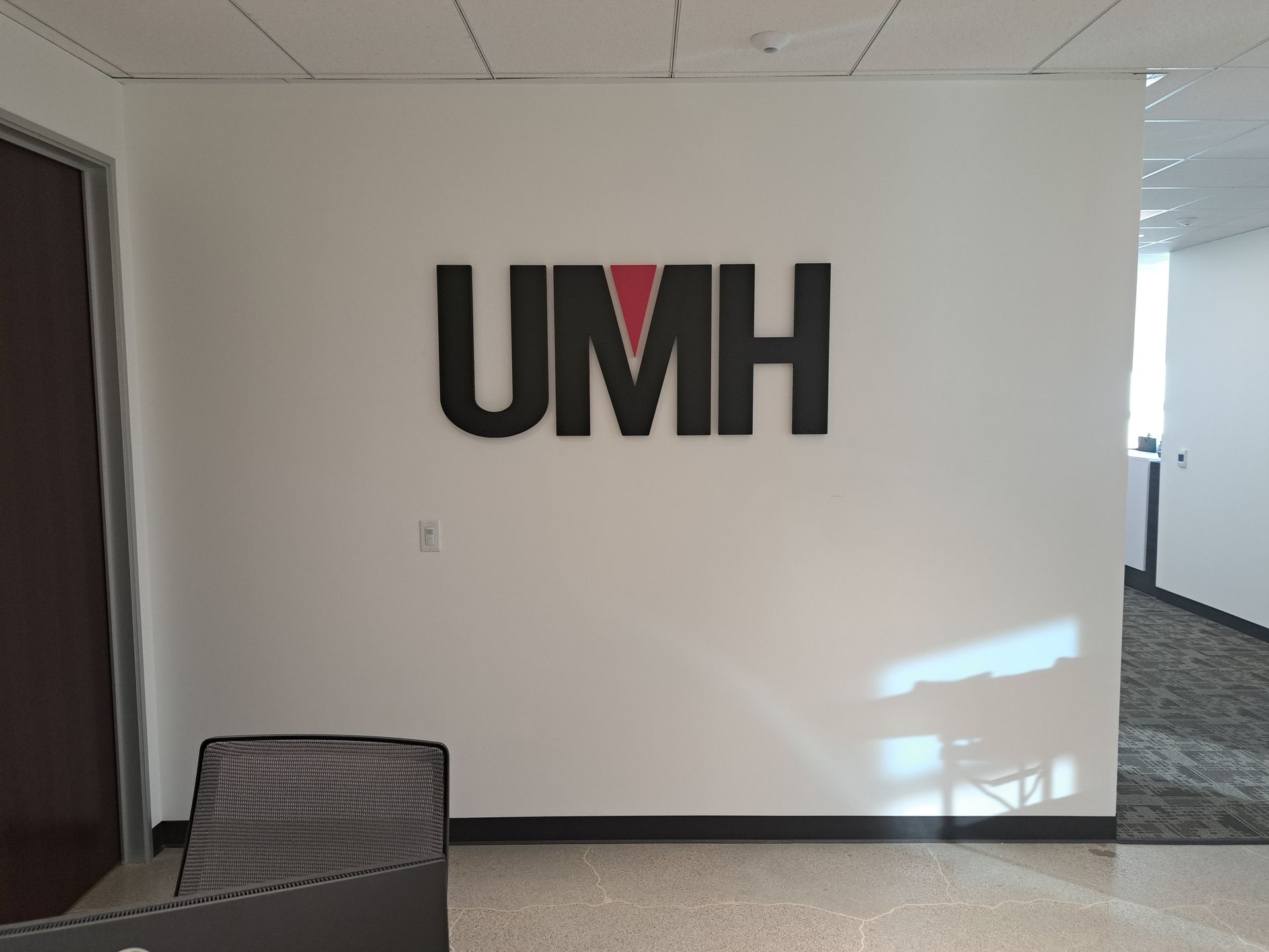 UMH logo on a white office wall beside a chair and hallway carpet