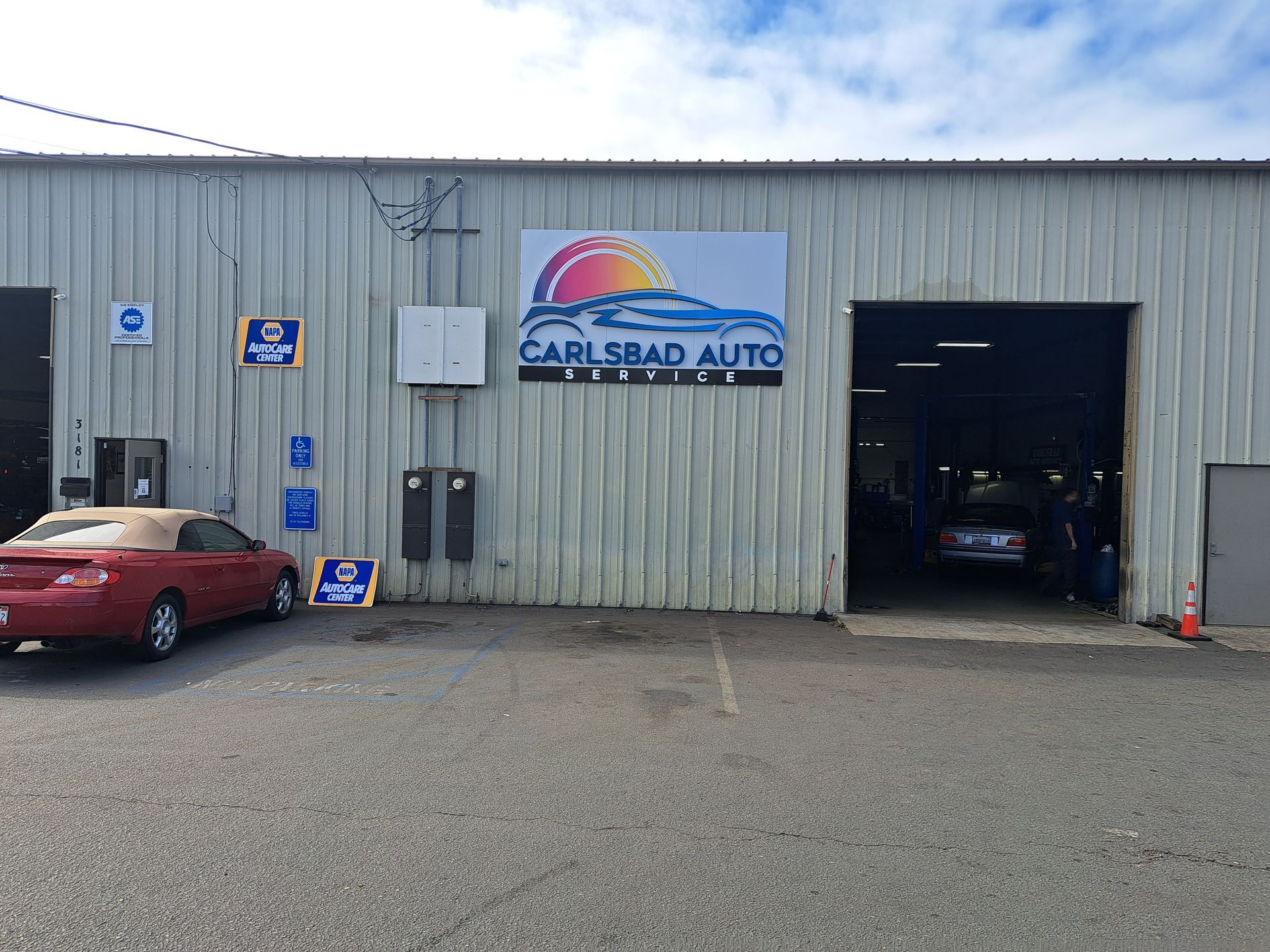 Carlsbad Auto garage exterior with a red car parked outside and an open service bay inside