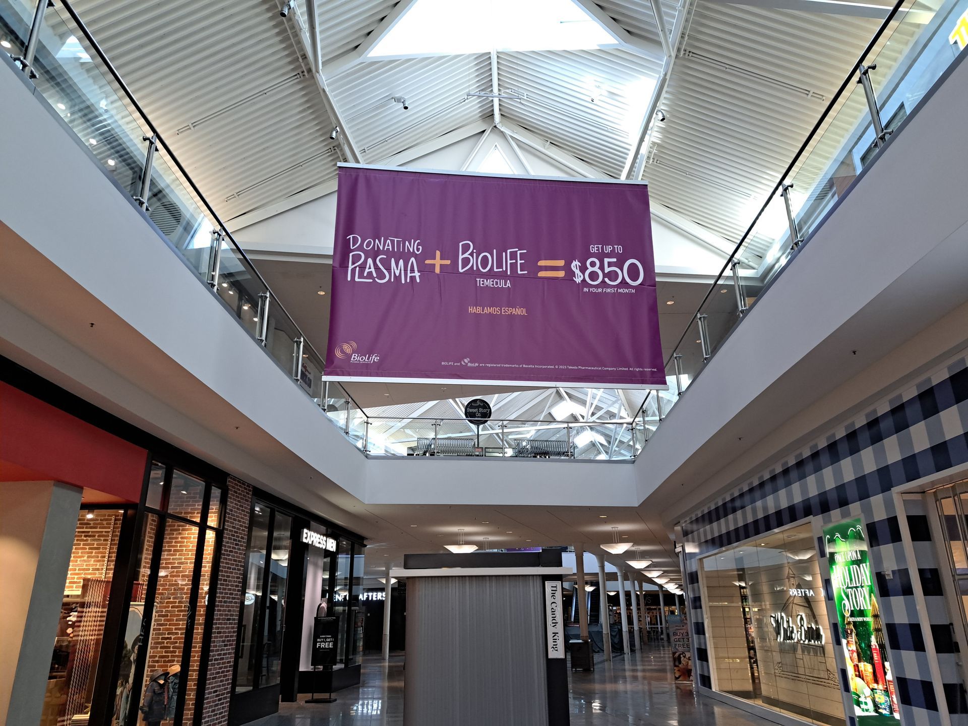 Shopping mall atrium with a large purple sale banner hanging from the ceiling.