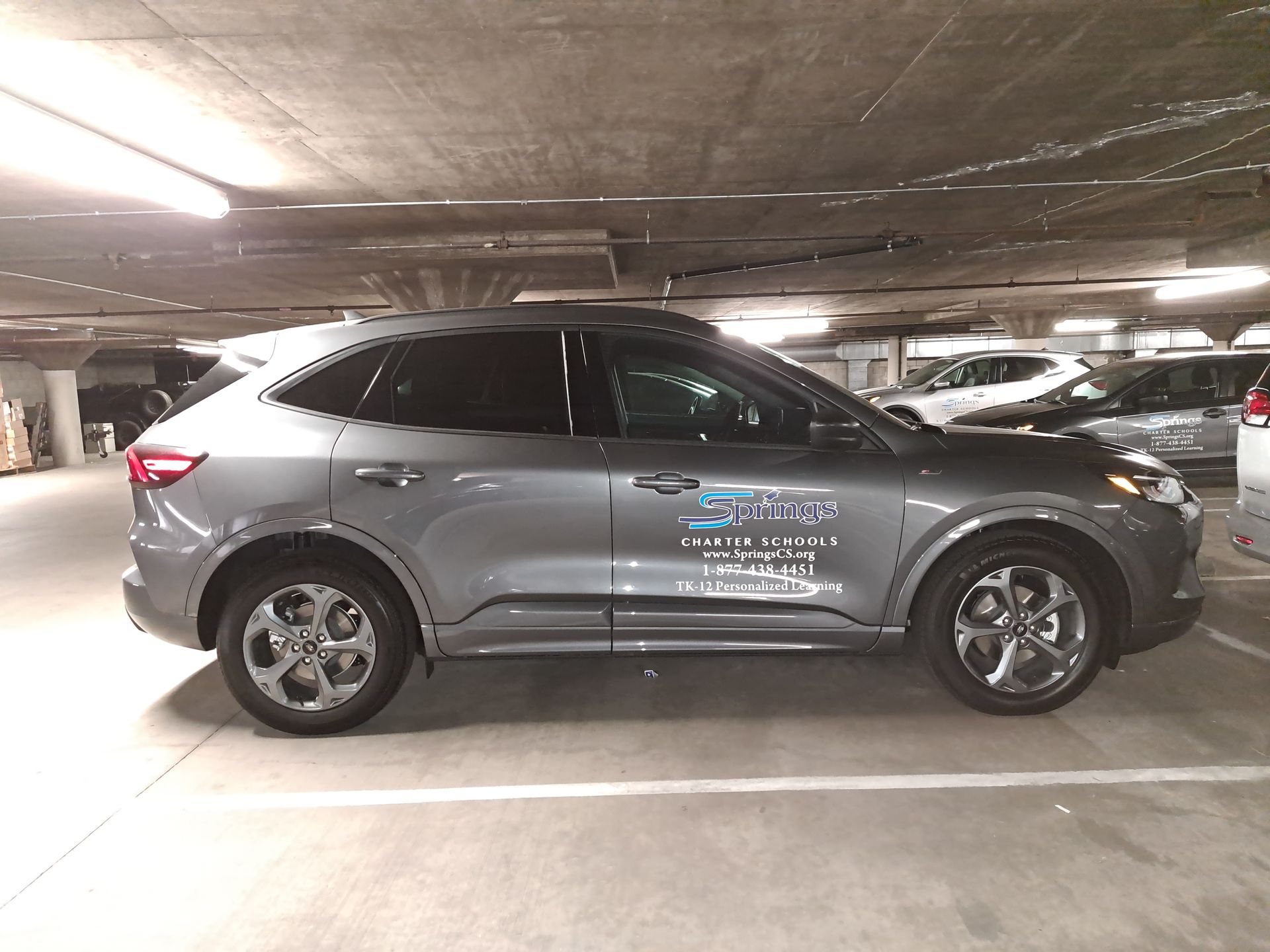 Gray SUV parked in an underground garage, side view with decals on the door.