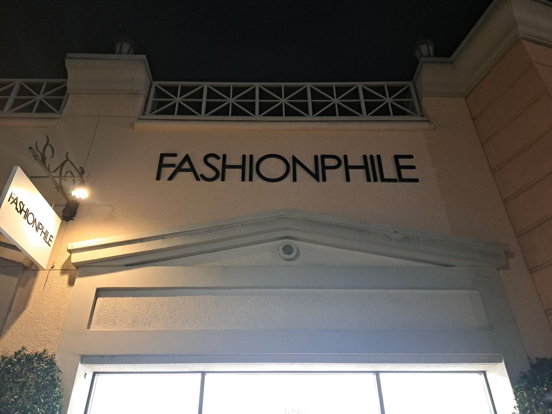 Storefront sign reading “FASHIONPHILE” above a brightly lit entrance at night