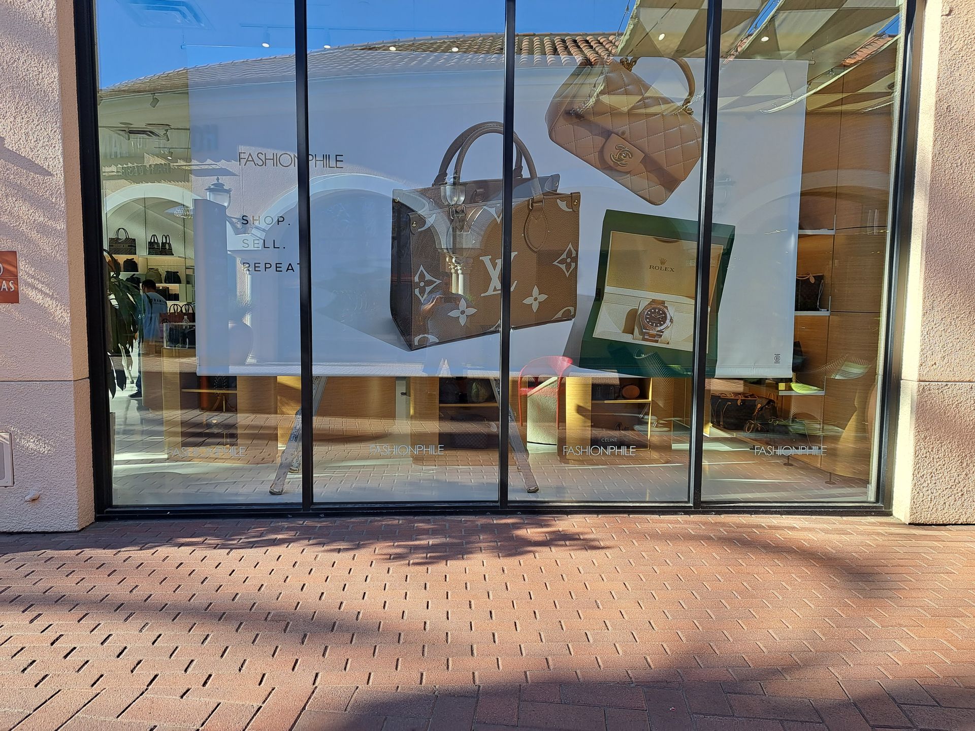 Storefront window display with large handbag posters and a brick walkway in front