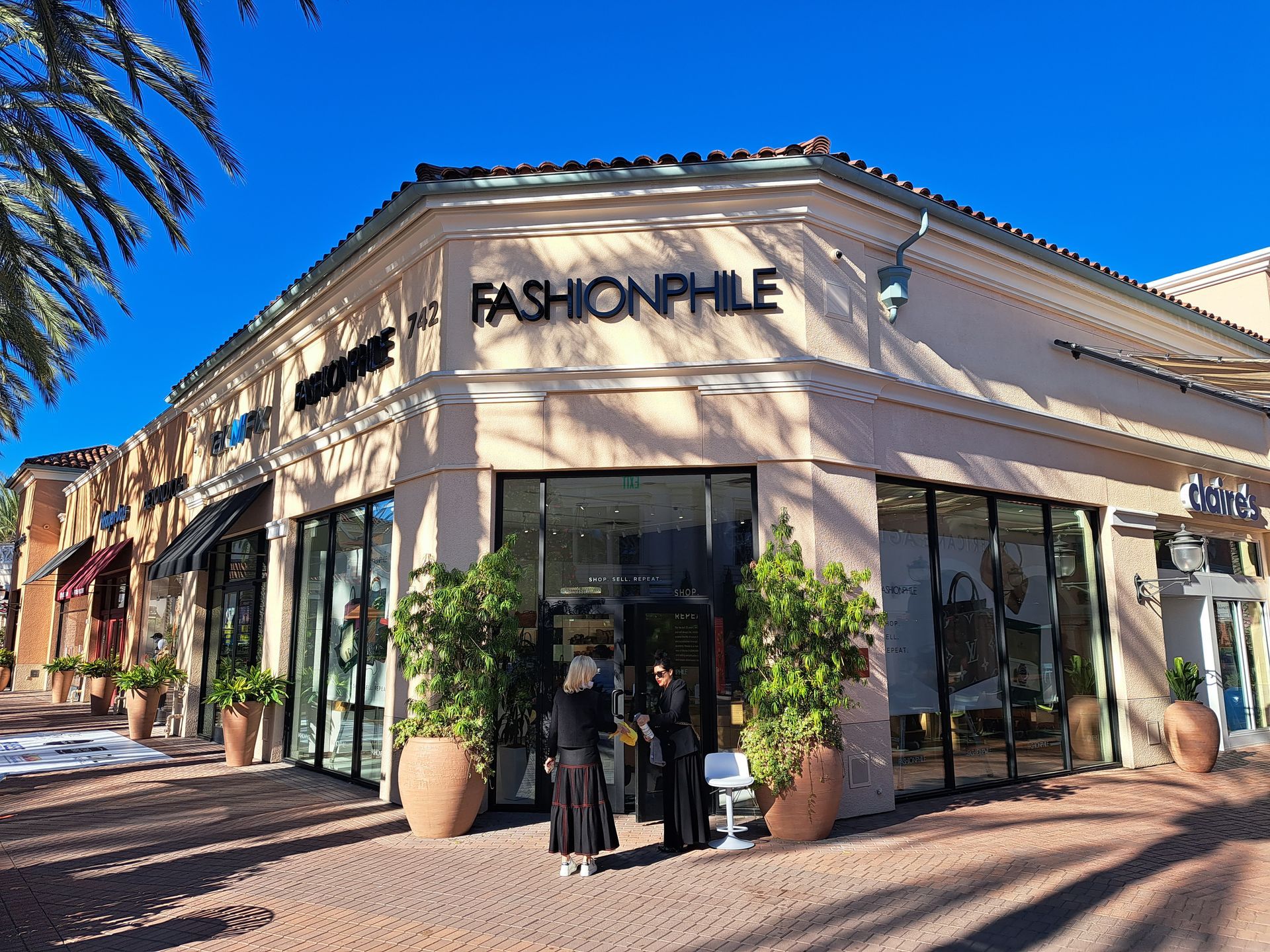 Fashionphile storefront on a sunny street with glass windows and potted plants