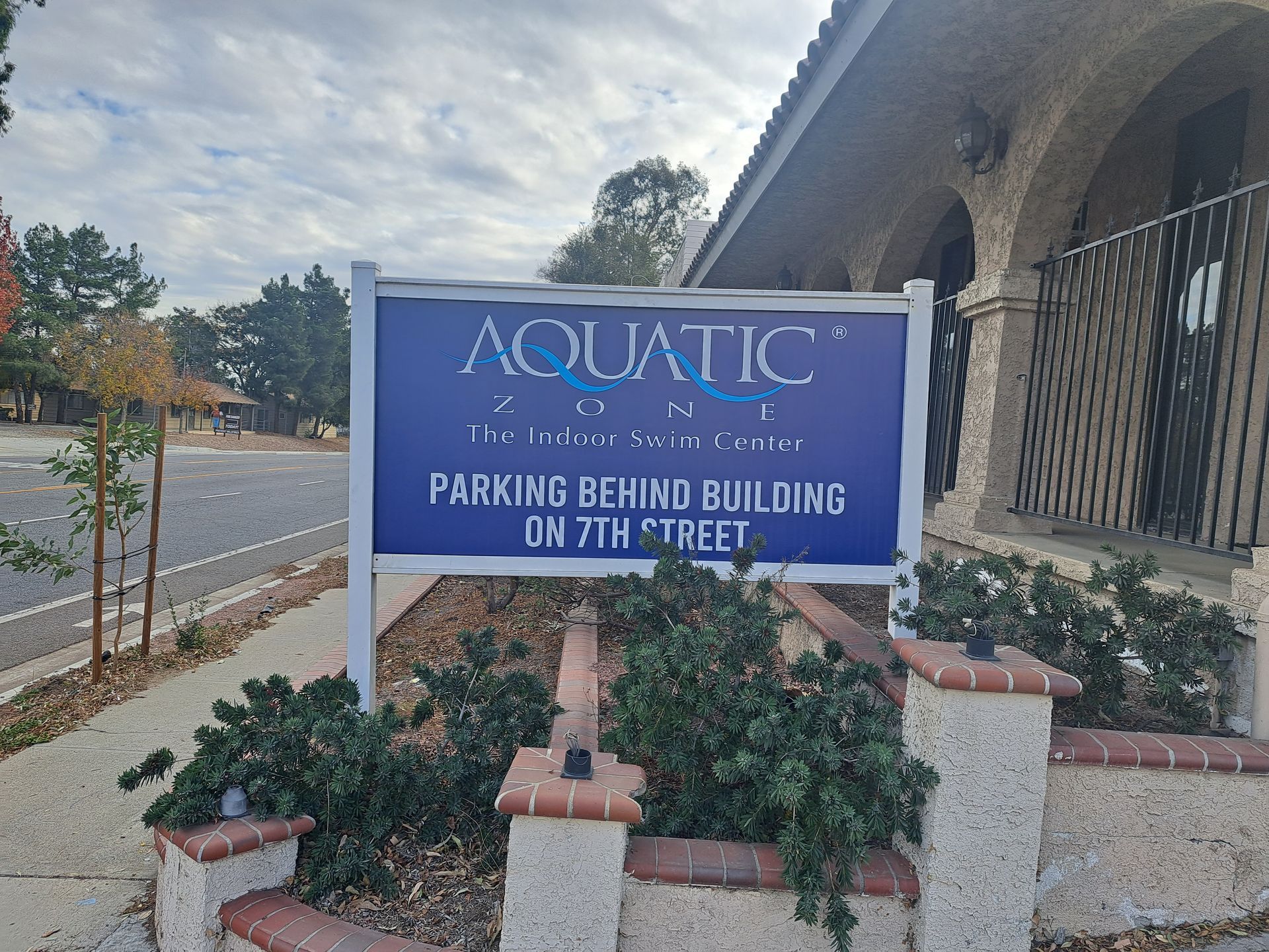 Blue Aquatic sign by a building, with brick planters and text directing parking behind the building on 7th Street