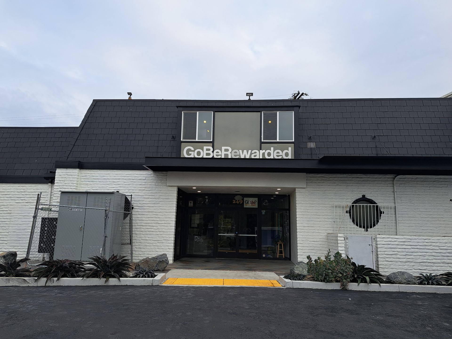 Front view of a white GoBeRewarded storefront with a black roof and entrance under an overcast sky