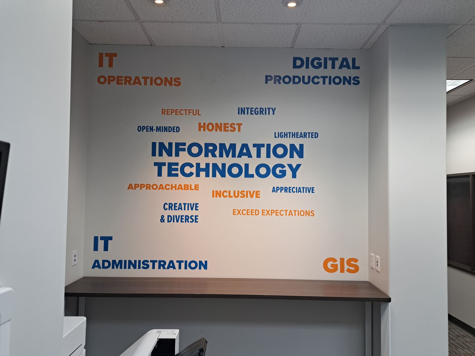 Wall mural of IT and digital information technology words in orange and blue on a gray office wall
