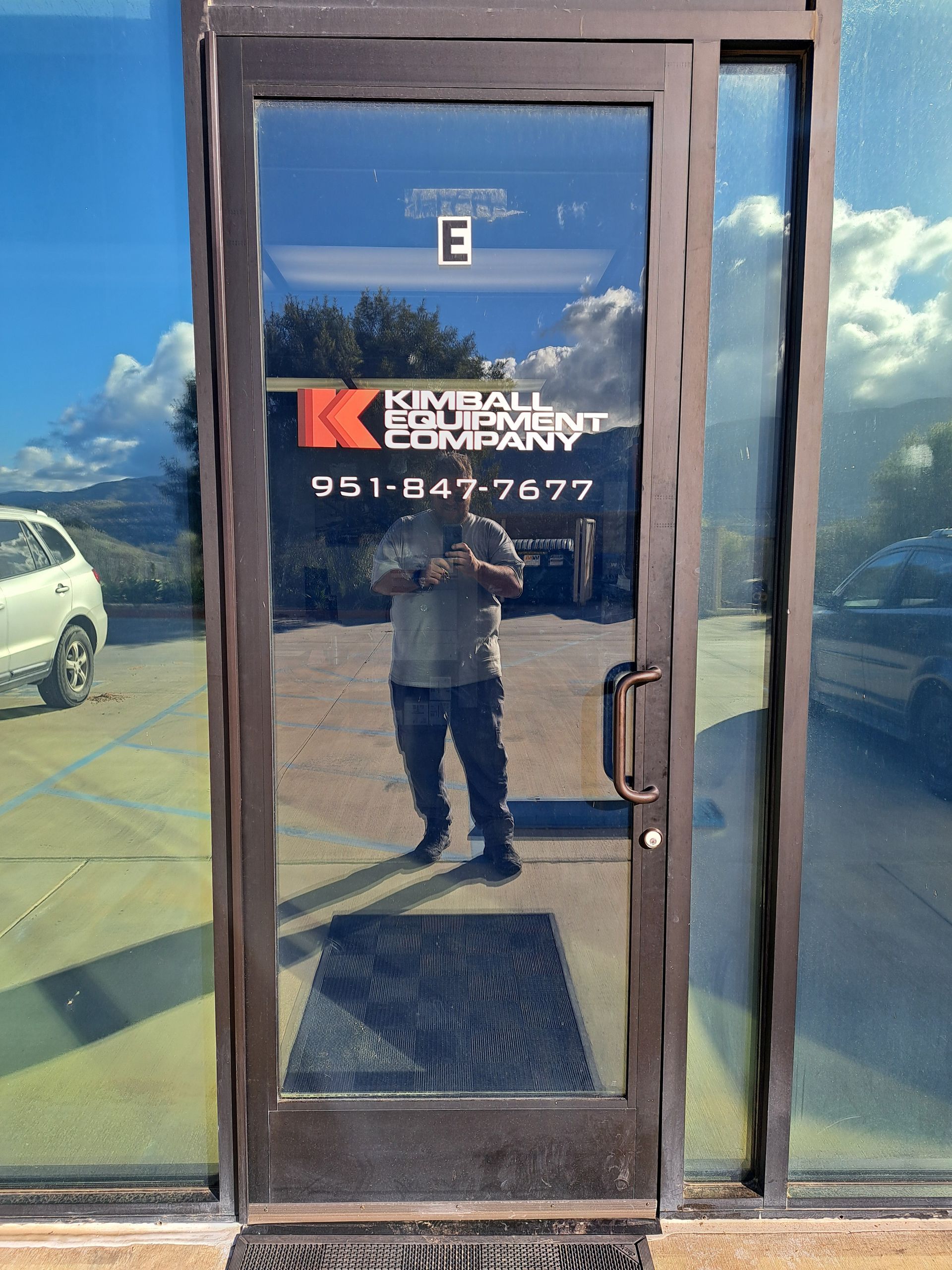 Glass storefront door with company logo, “E” sign, and phone number 951-847-7077 reflected in the glass
