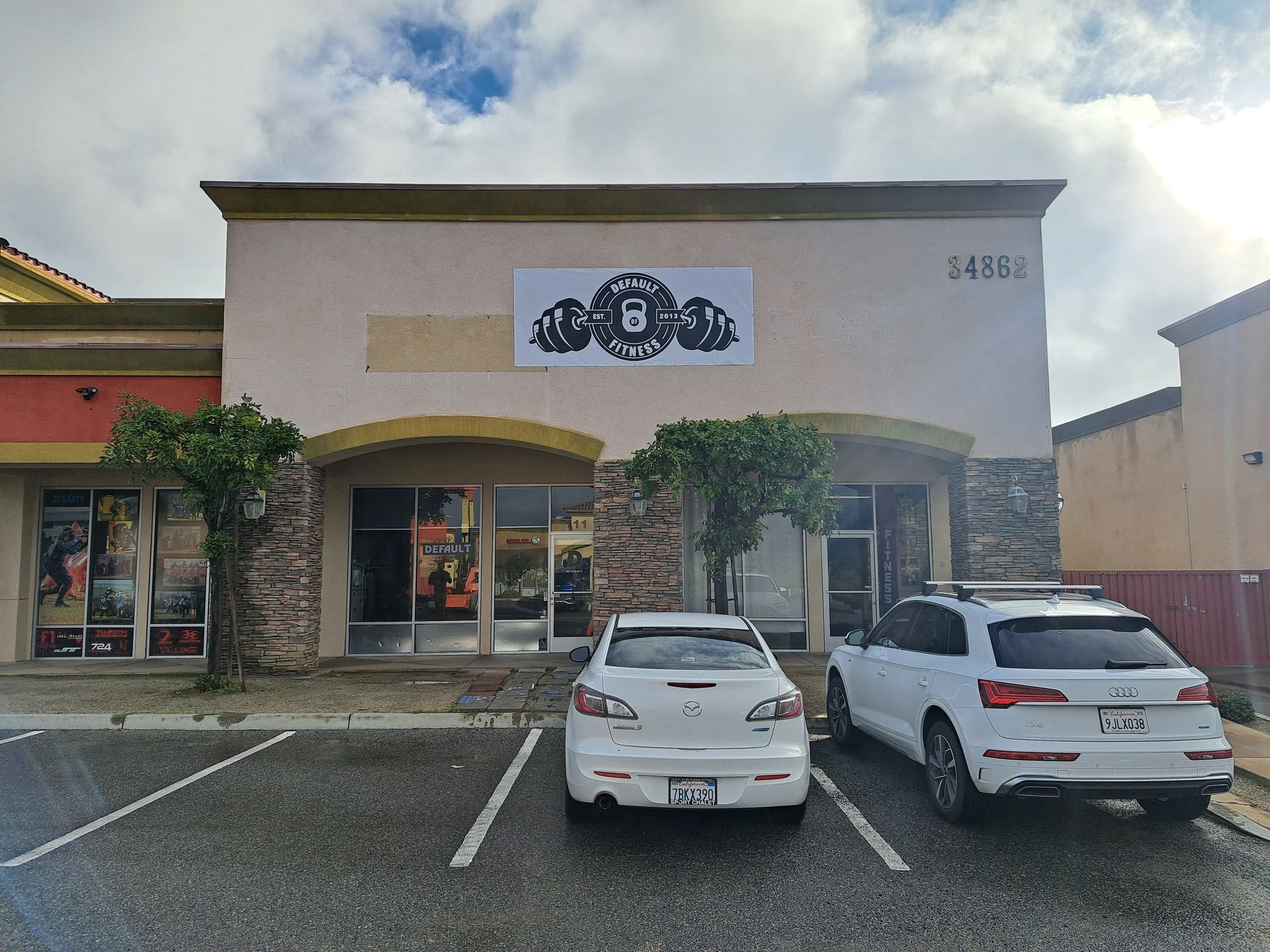Shopping center storefront with parked white cars and a decorative sign above the entrance