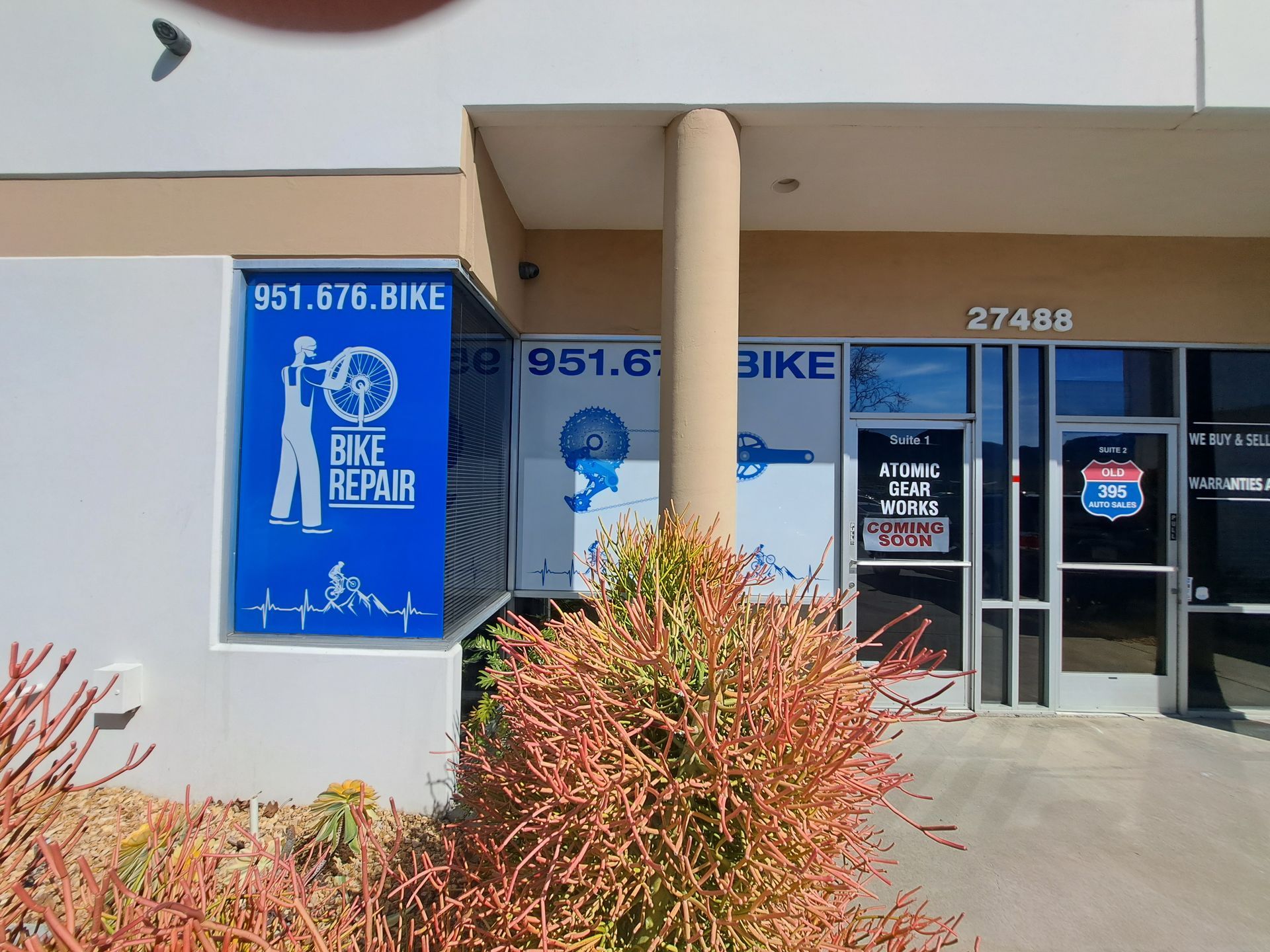 Bike Repair storefront with blue sign, glass door, and orange shrubs outside.