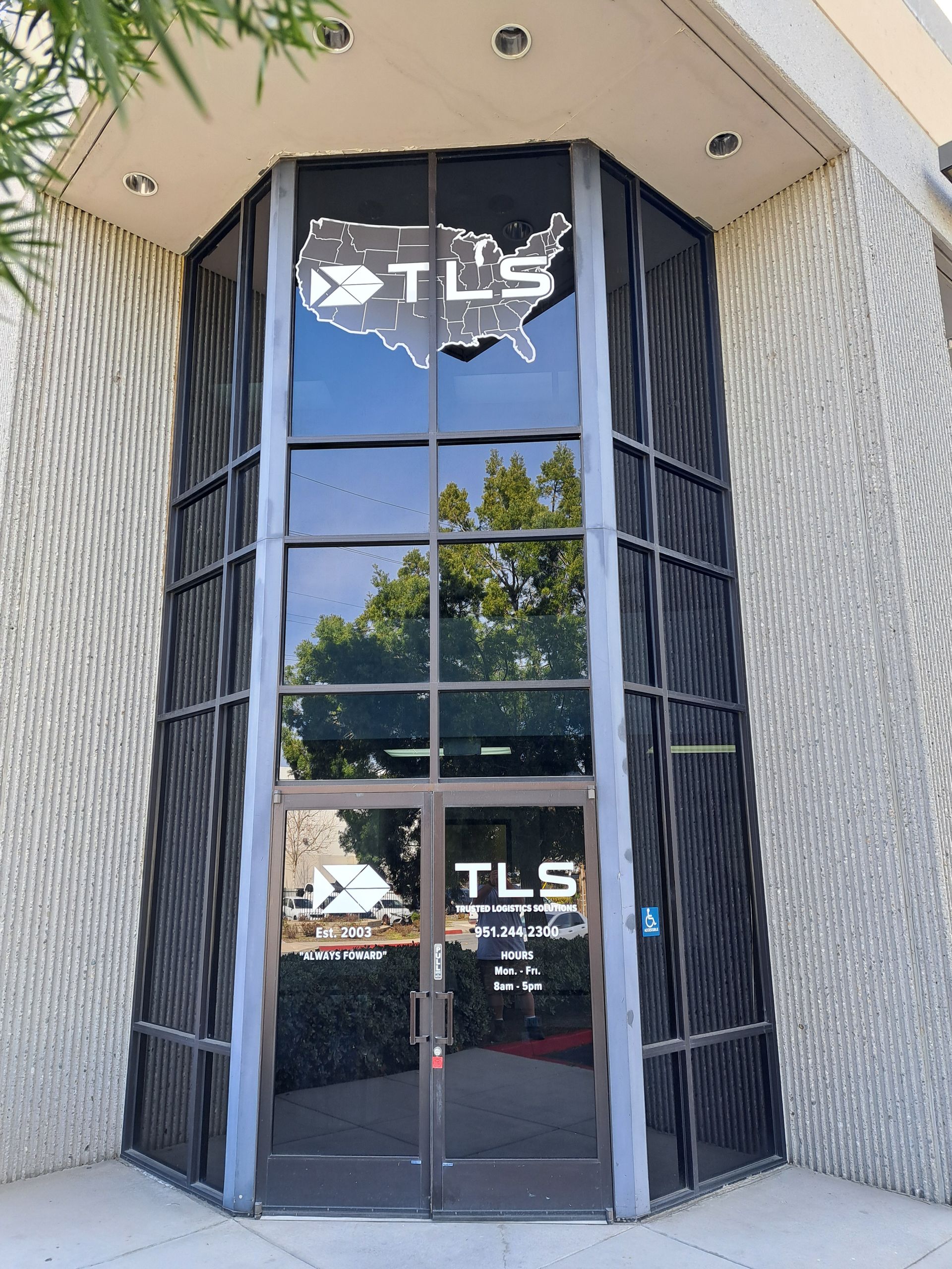 Glass storefront entrance with TLS logo and reflective doors in a concrete building facade