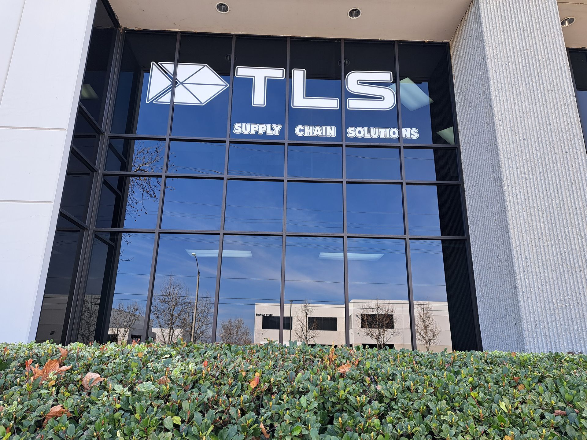 TLS Supply Chain Solutions office entrance with reflective glass and shrubs in front