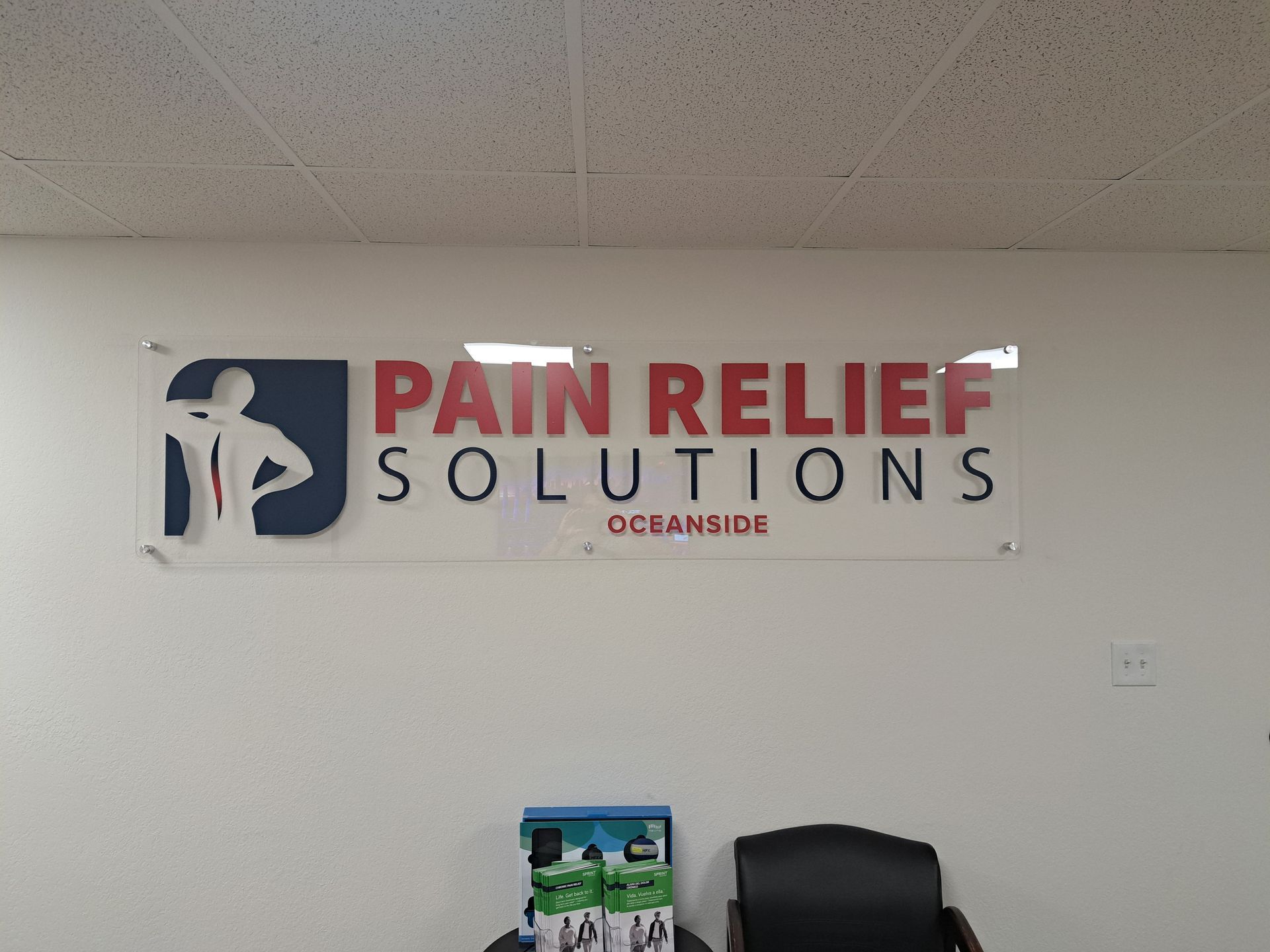 Pain Relief Solutions sign on a white wall above a chair in a clinic waiting area