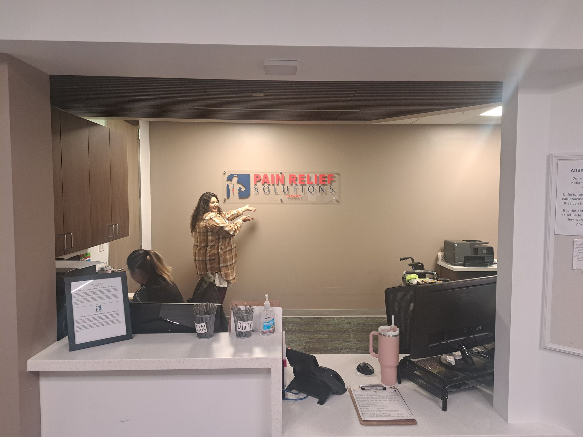Pain Relief Center reception area with staff arranging a wall sign behind the front desk
