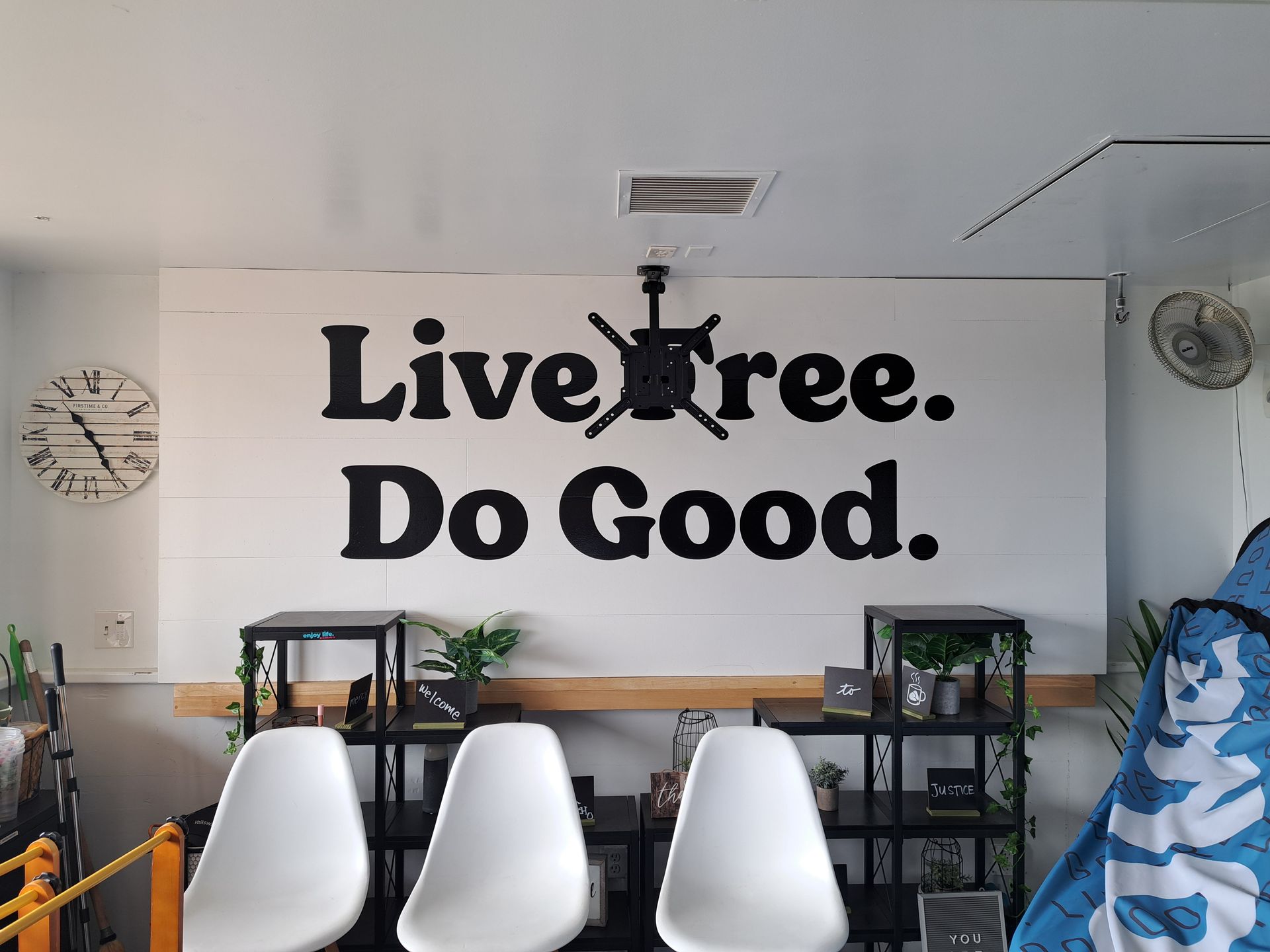Office wall mural reading “Live tree. Do Good.” above chairs and shelves