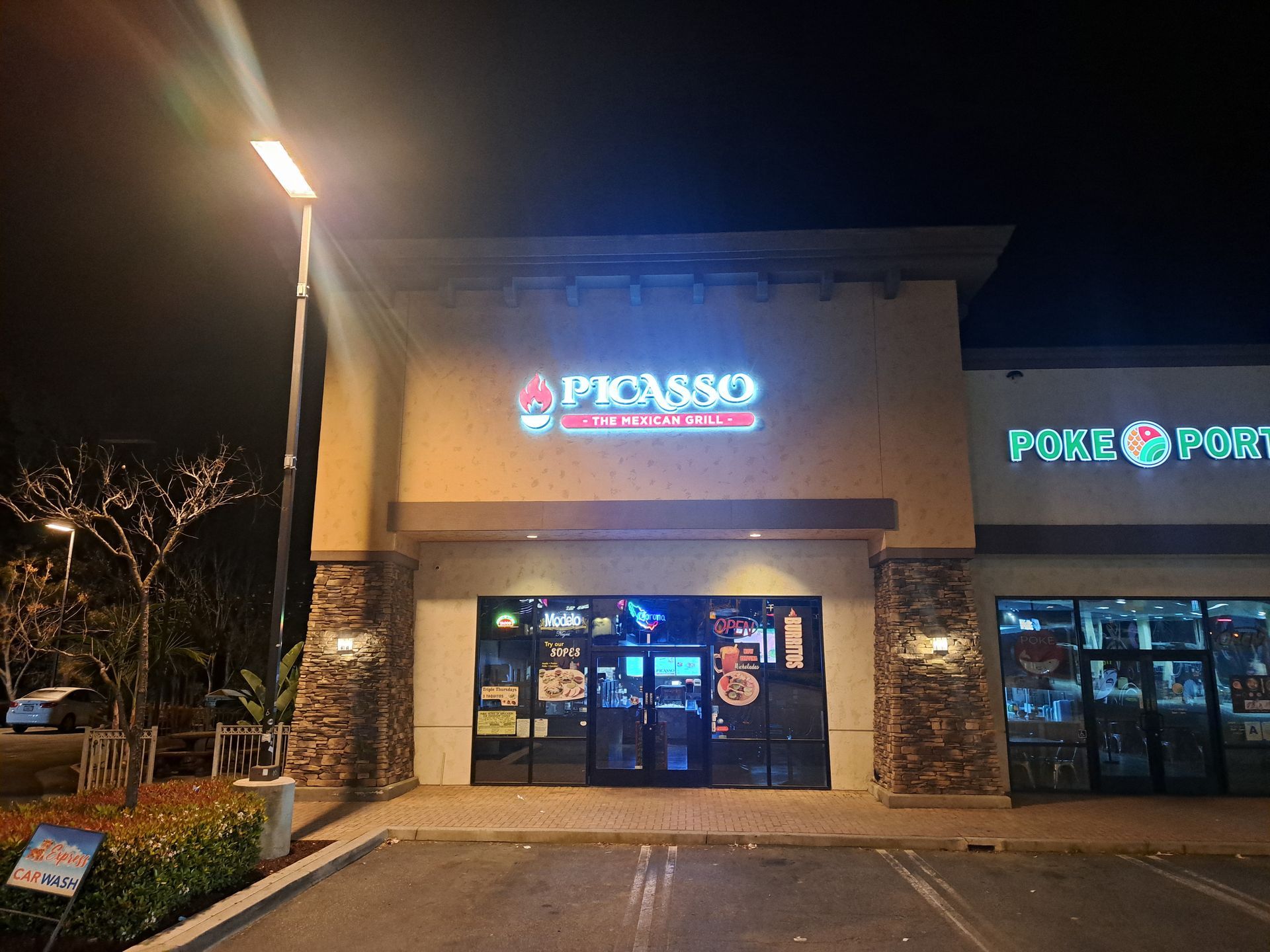 Nighttime exterior of a Pizzasso restaurant with bright neon signs and glass entrance doors