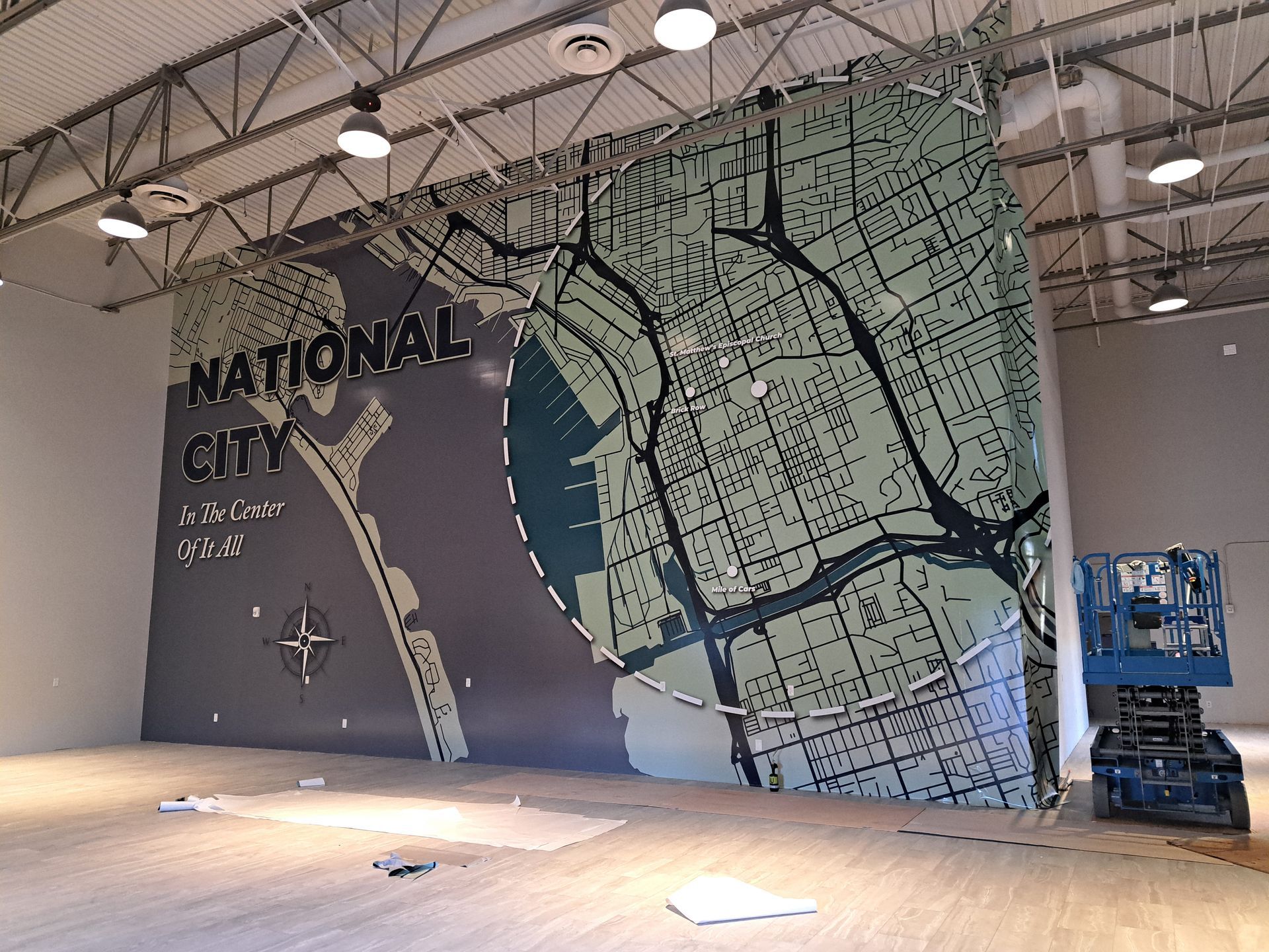 Large mural map on a warehouse wall with “NATIONAL CITY” text and a blue industrial lift nearby