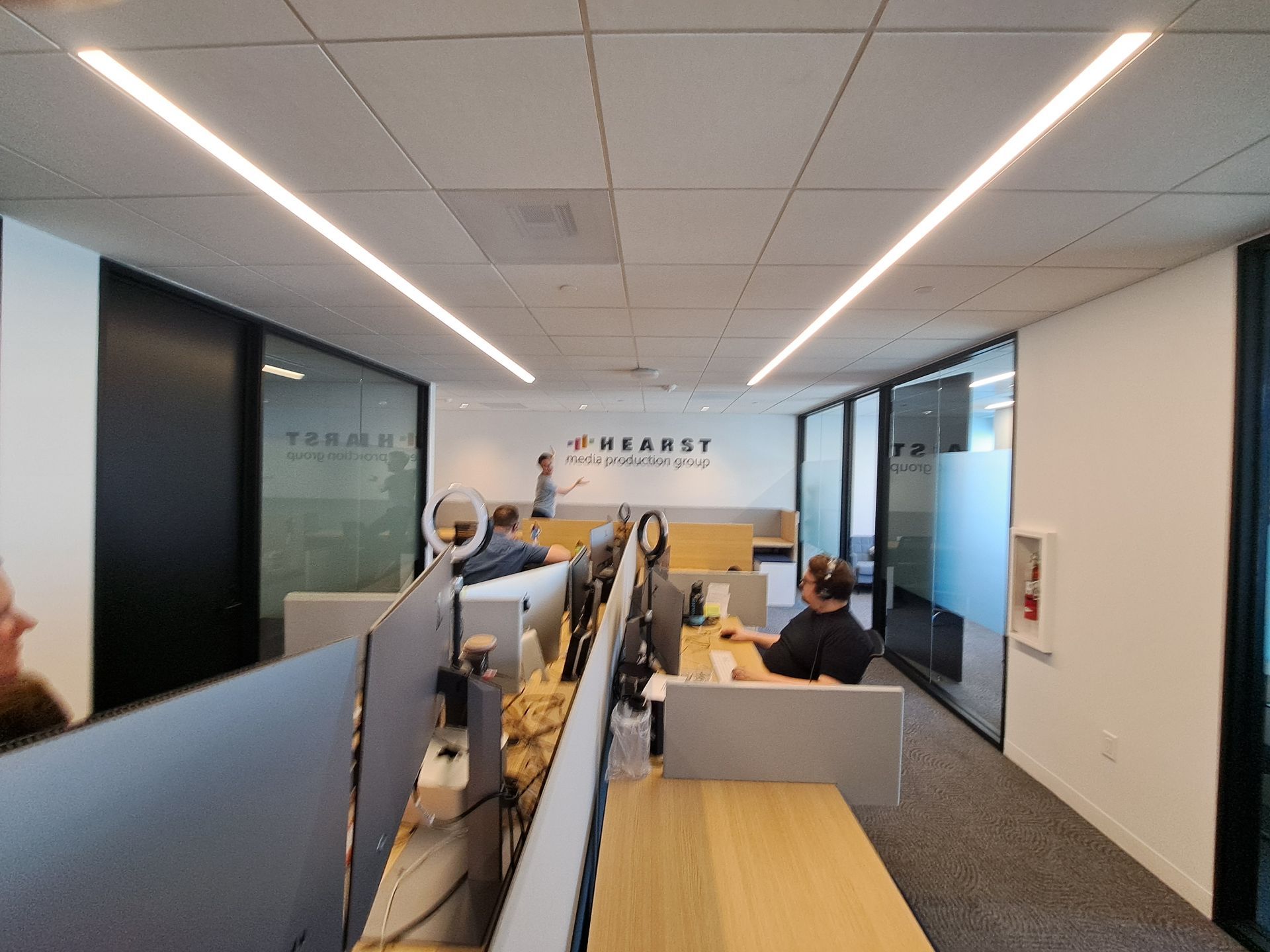 Modern office corridor with desks, glass walls, and people working at computers