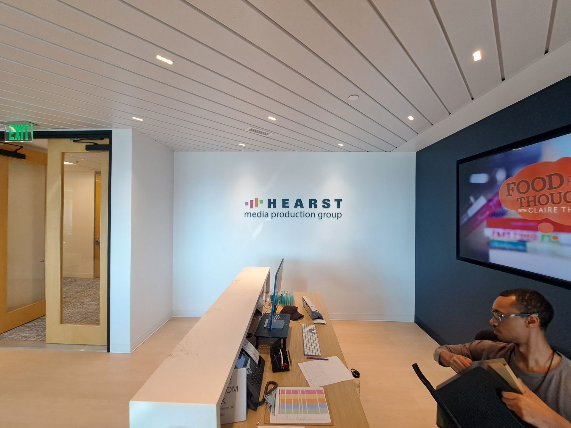 Modern office lobby with a reception desk, wall logo, and a seated person using a laptop