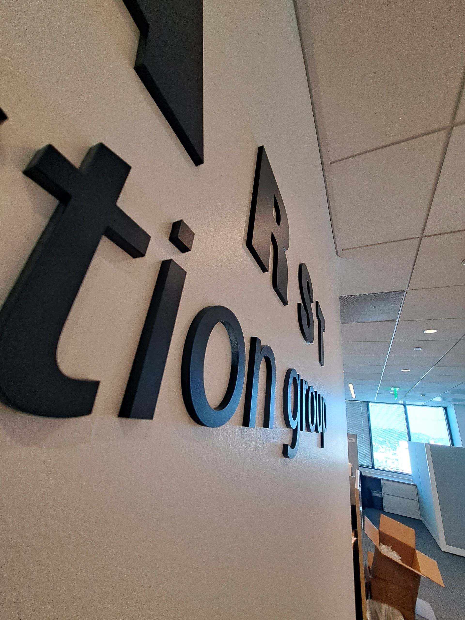 Tilted view of a hallway wall with the black “triom…” logo and bright office corridor beyond