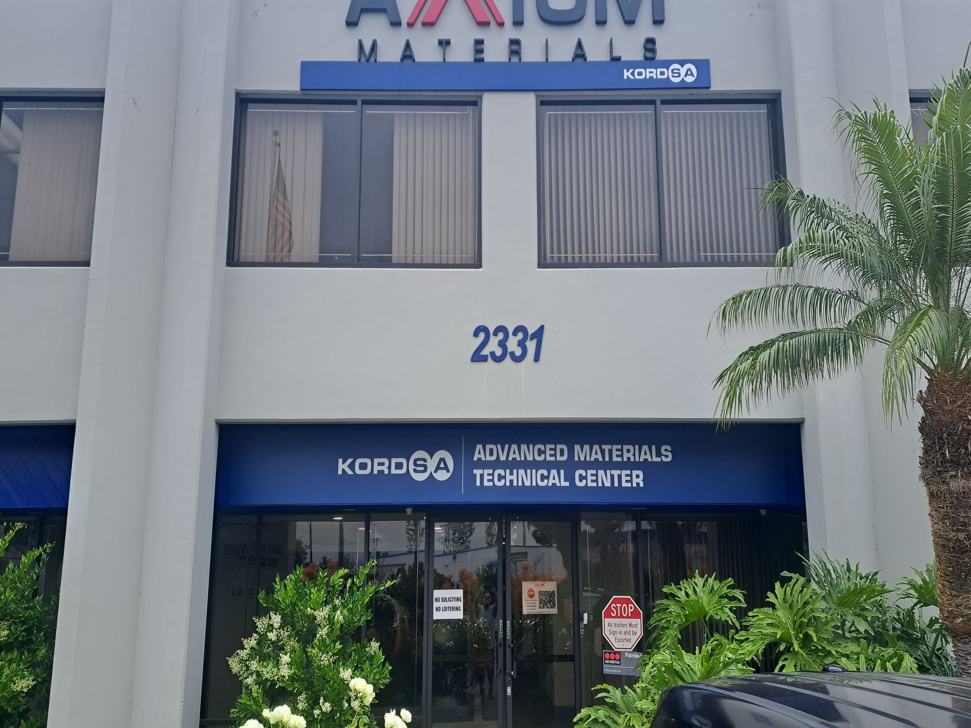 Facade of a white two-story building with a blue Awash Material Technical Center sign and entrance doors.