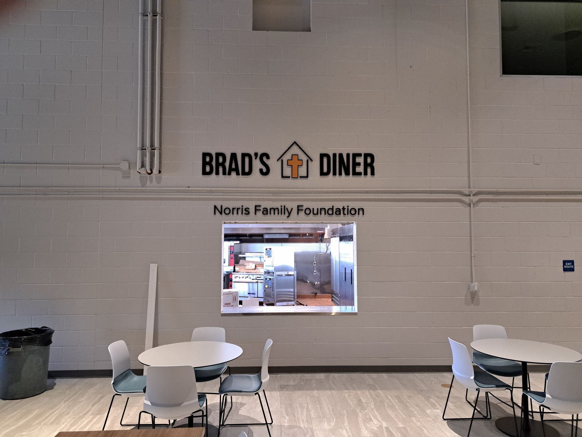 Interior wall of Brad’s Diner with a service window and tables in a mostly empty dining area.