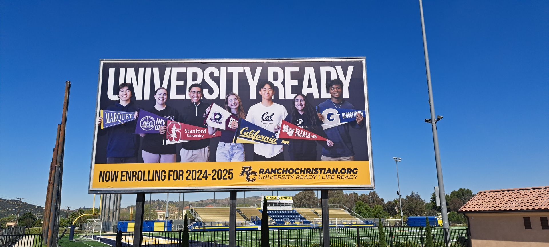 Large roadside billboard reading “University Ready” under a bright blue sky.
