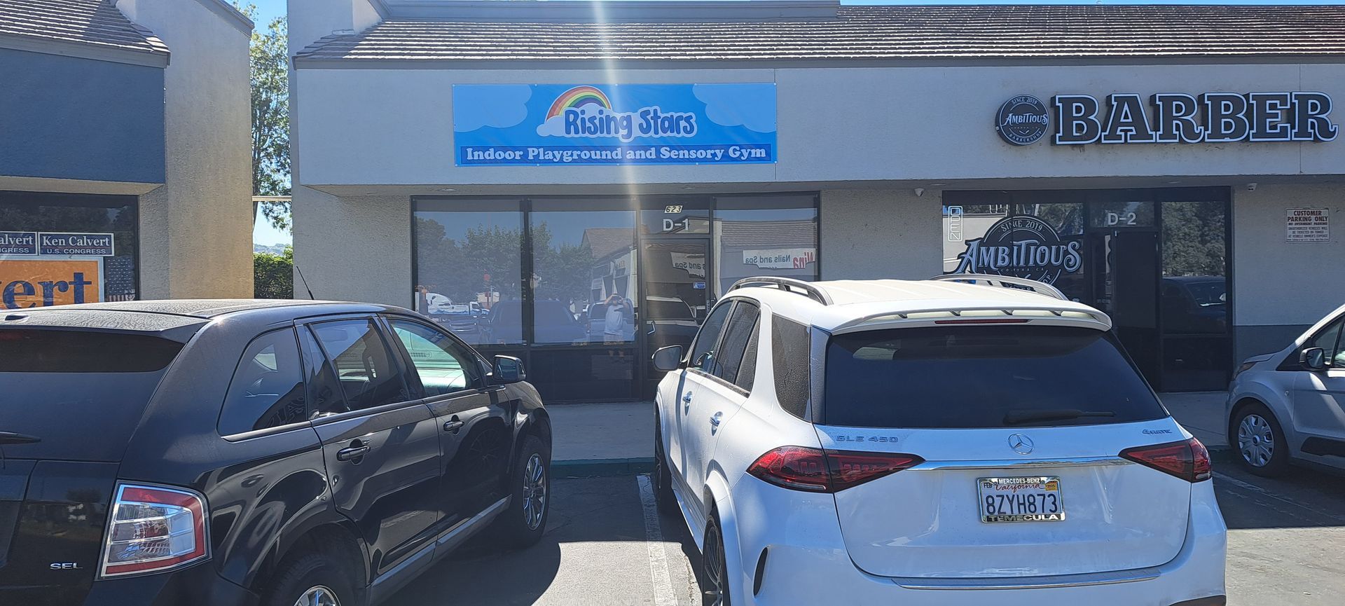 Storefront with parked black and white SUVs in front, including a sign for a barber shop.
