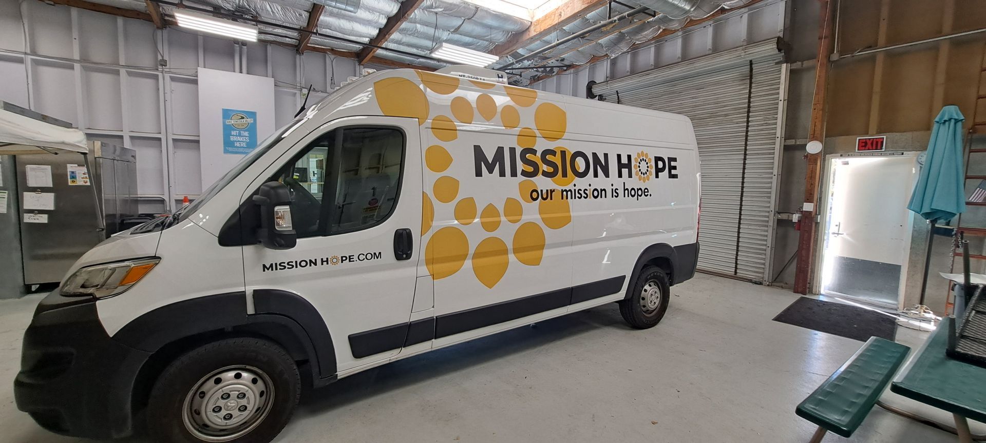 White Mission Hope van parked inside a warehouse-like garage, with orange logo graphics on the side.