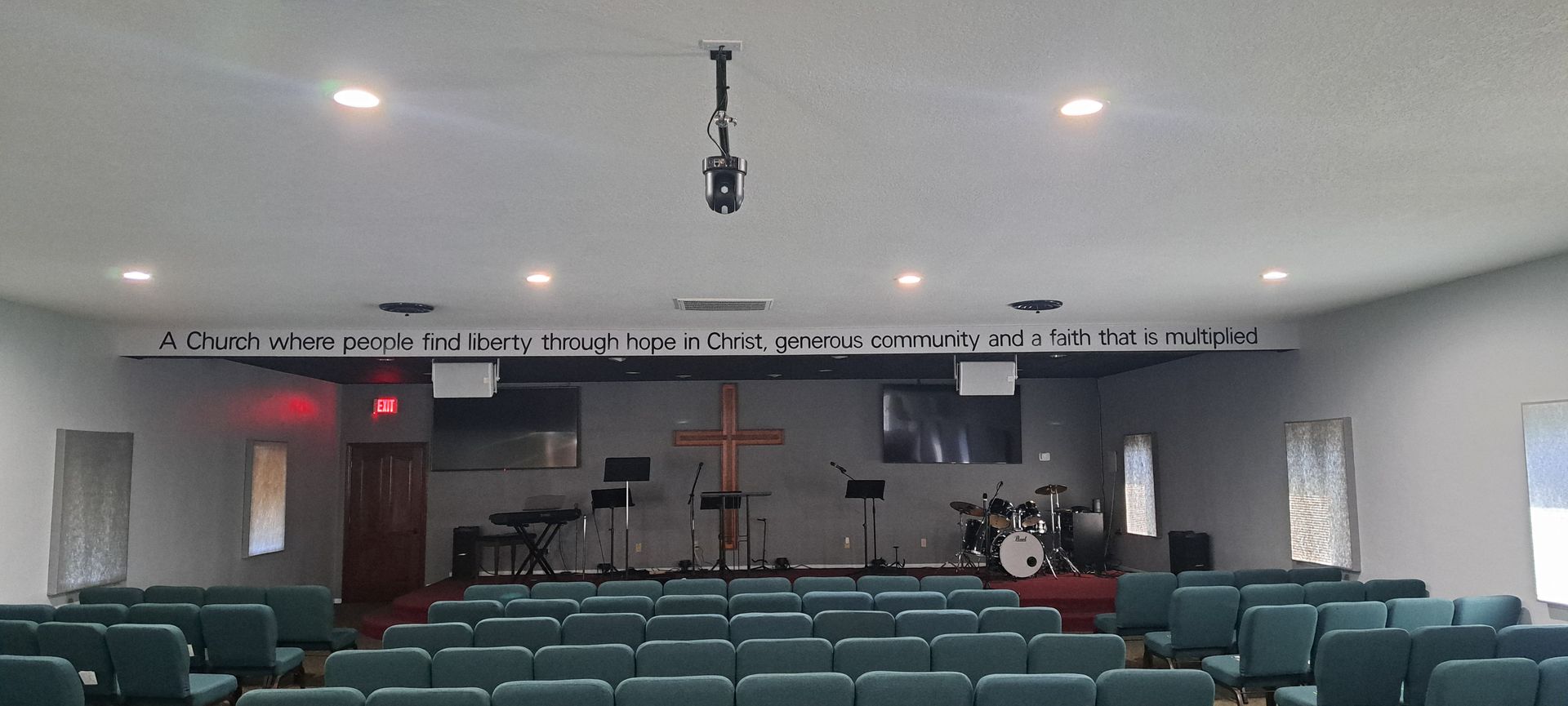 Wide view of an empty church sanctuary with green pews, a cross, and a drum set on the stage