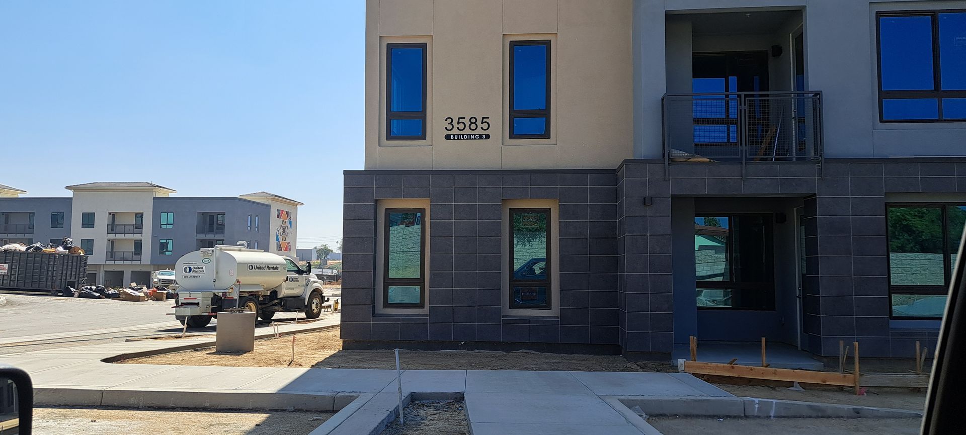Modern apartment building exterior with parked pickup truck and unfinished street landscaping
