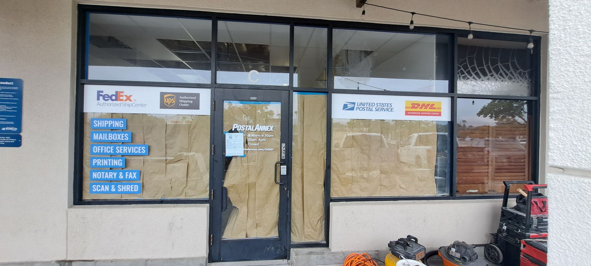 Closed storefront with taped windows and door, FedEx sign, and boxes piled outside.
